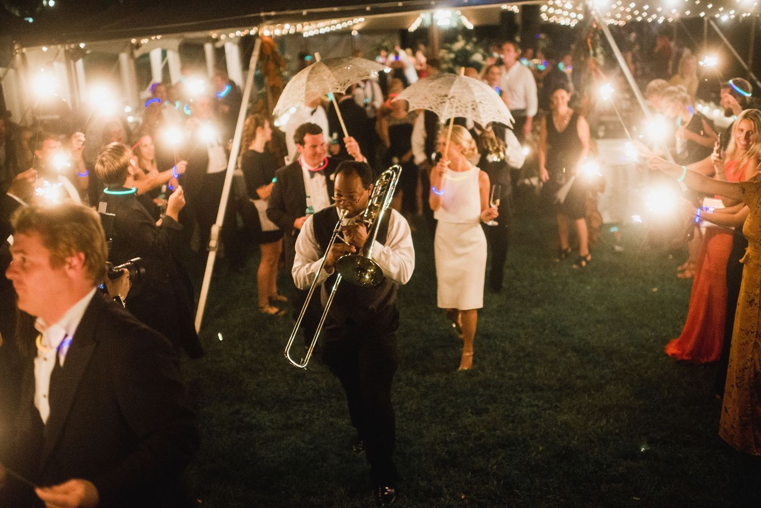 Wedding guests hold sparklers creating a magical light tunnel during an outdoor nighttime celebration.