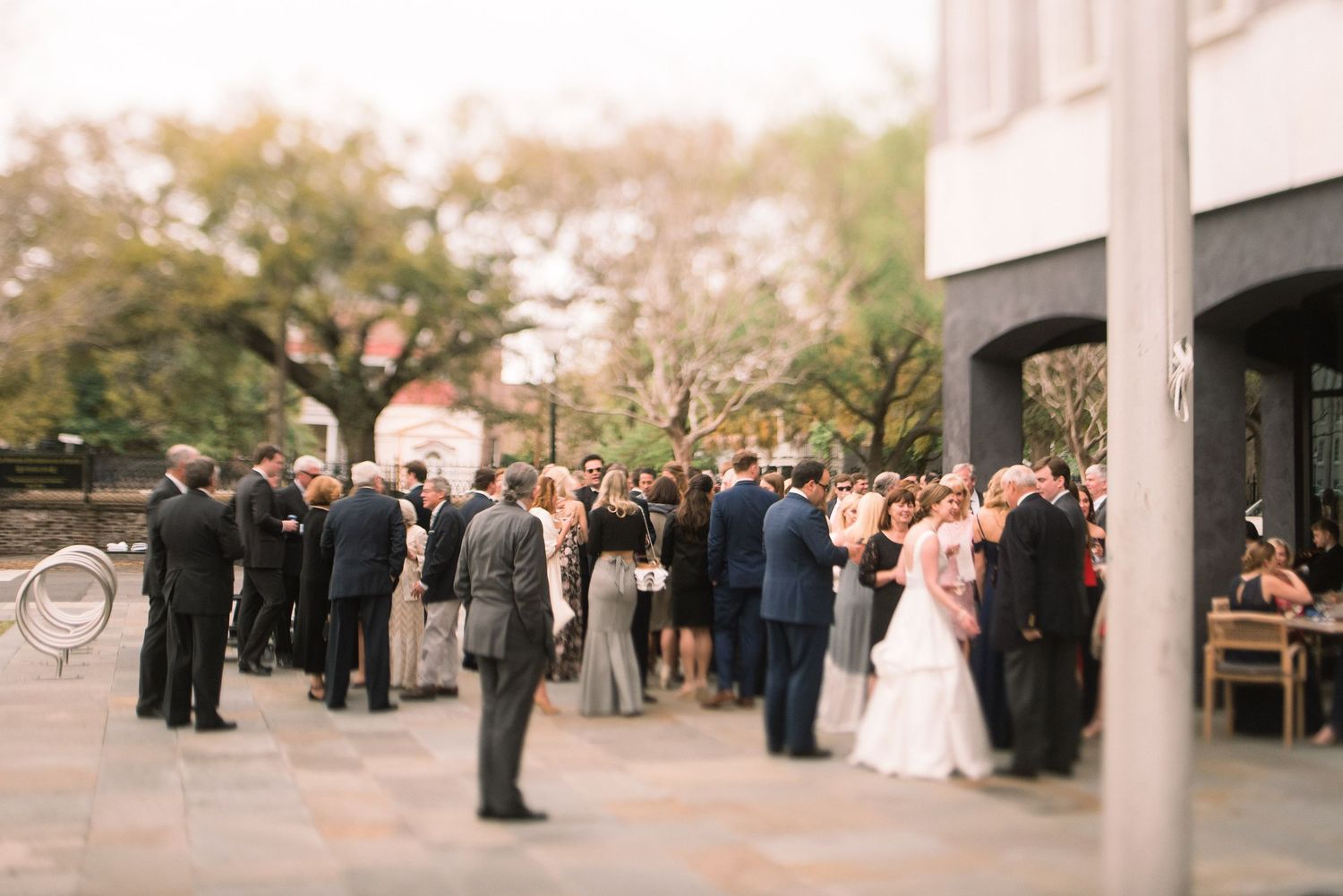 Wedding guests gather outdoors under white pillars during a sunset ceremony at an elegant venue.