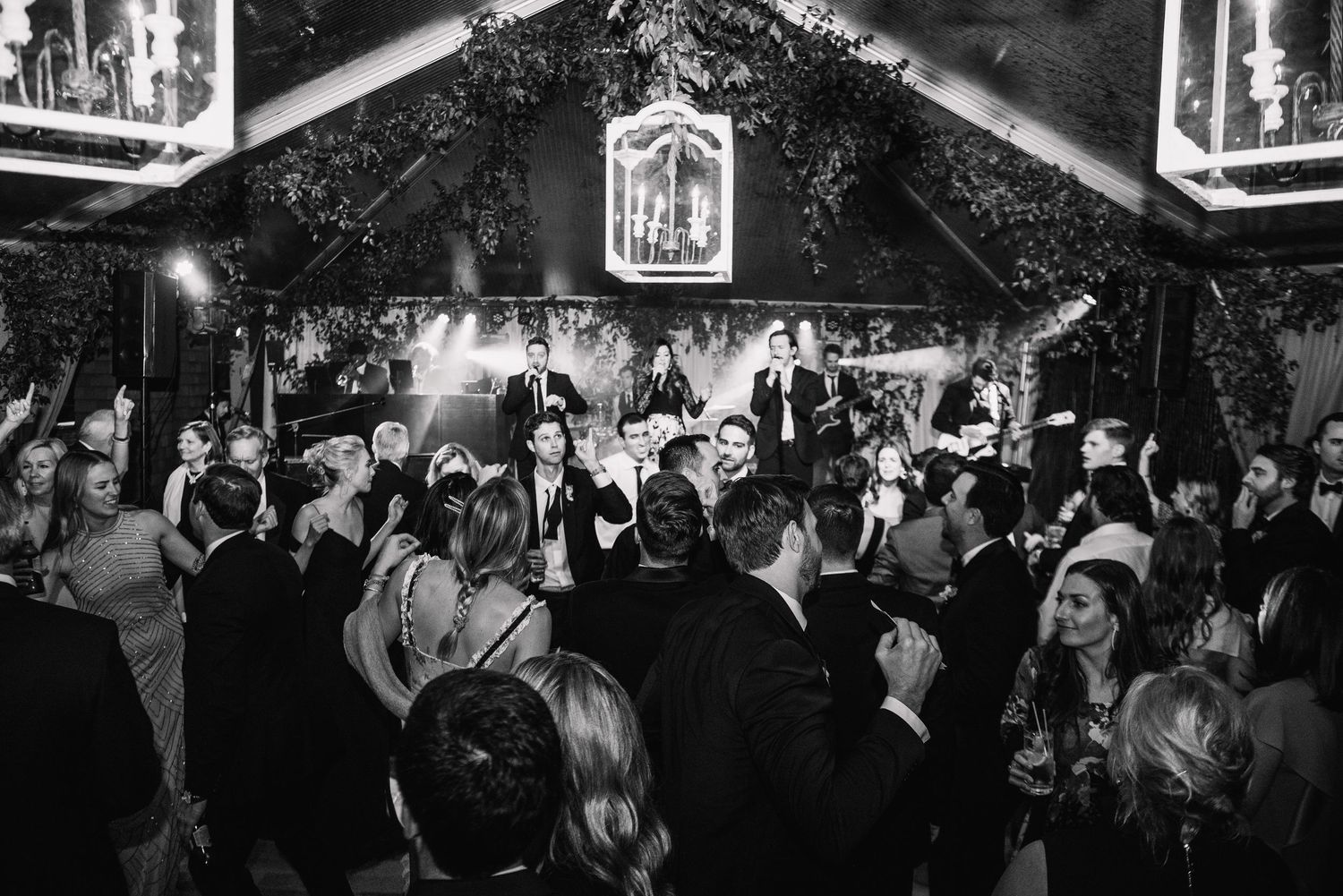 A crowded dance floor filled with people celebrating at a wedding reception under decorative lighting.