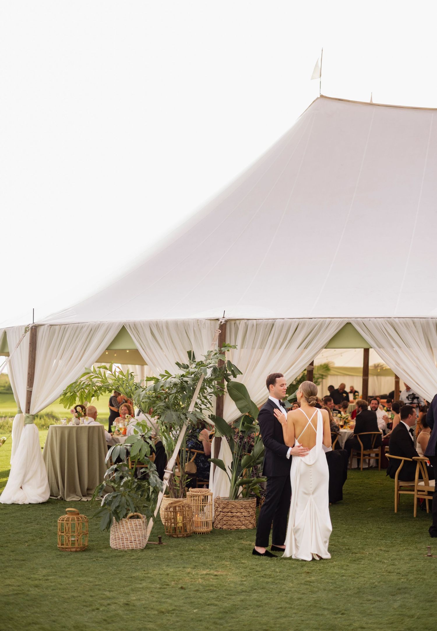 A series of elegant white wedding tents set up on a lush green lawn with guests mingling and hay bale seating.