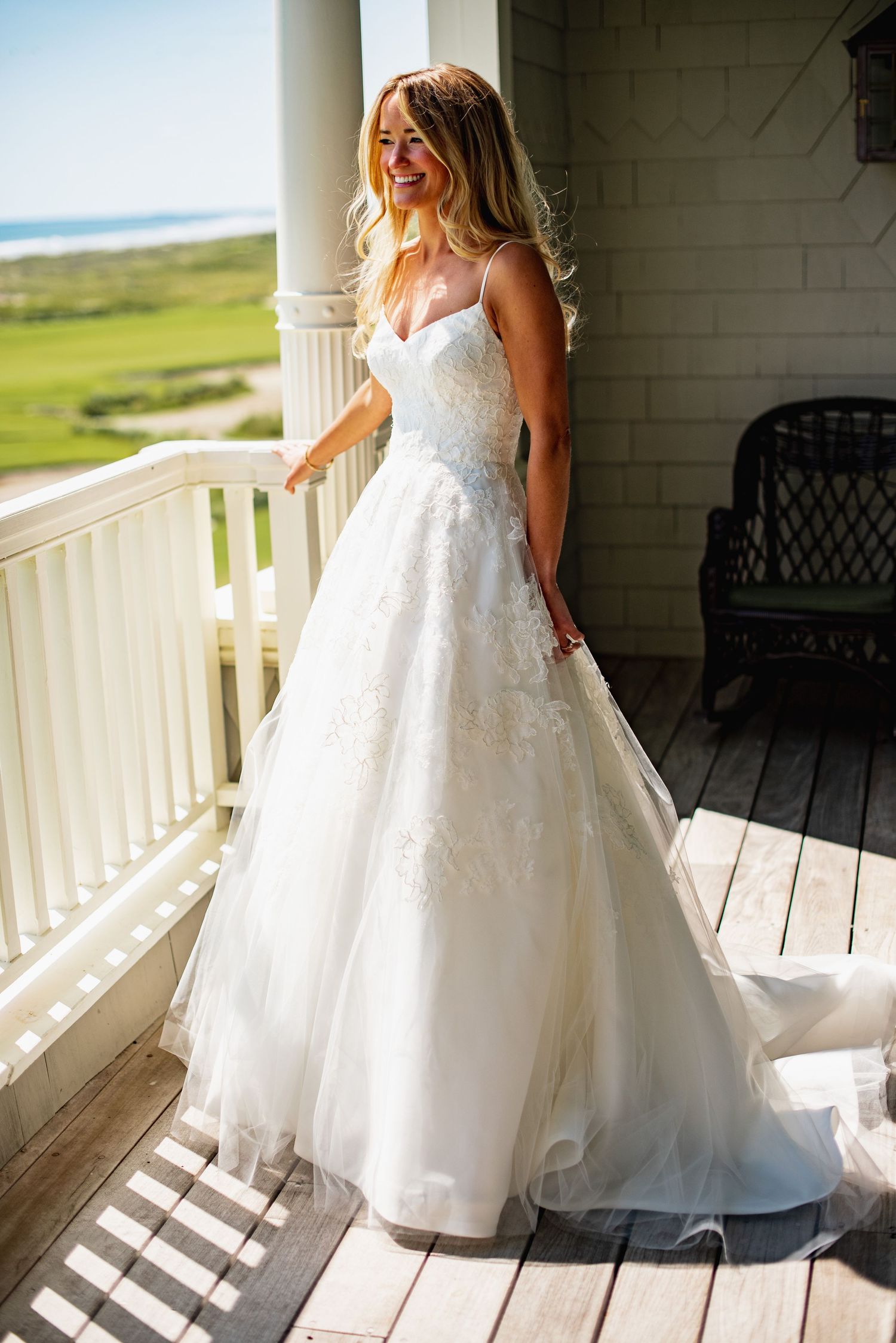 A flowing white wedding dress with lace details is shown in multiple angles on a bright porch with white columns.