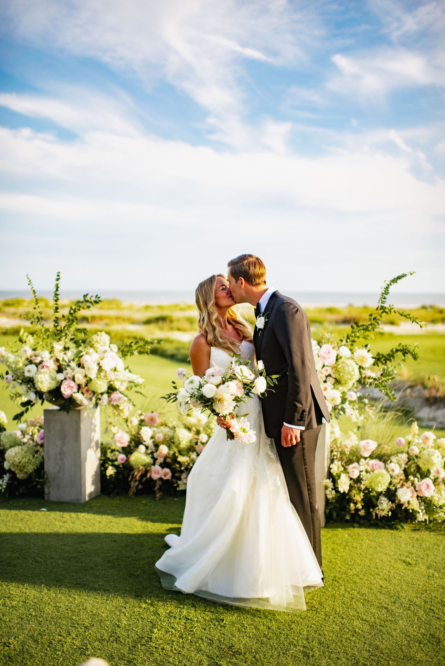 A romantic outdoor wedding ceremony on a lush green golf course with elegant white floral arrangements.