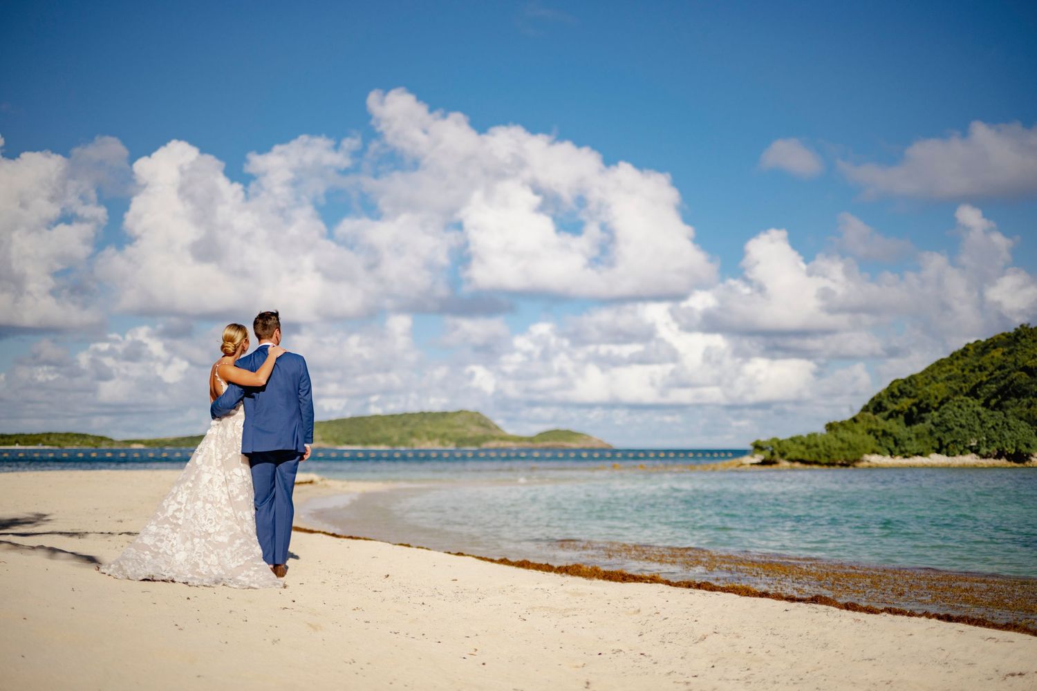 Panoramic view of a pristine beach wedding ceremony with turquoise waters and cloudy blue skies.