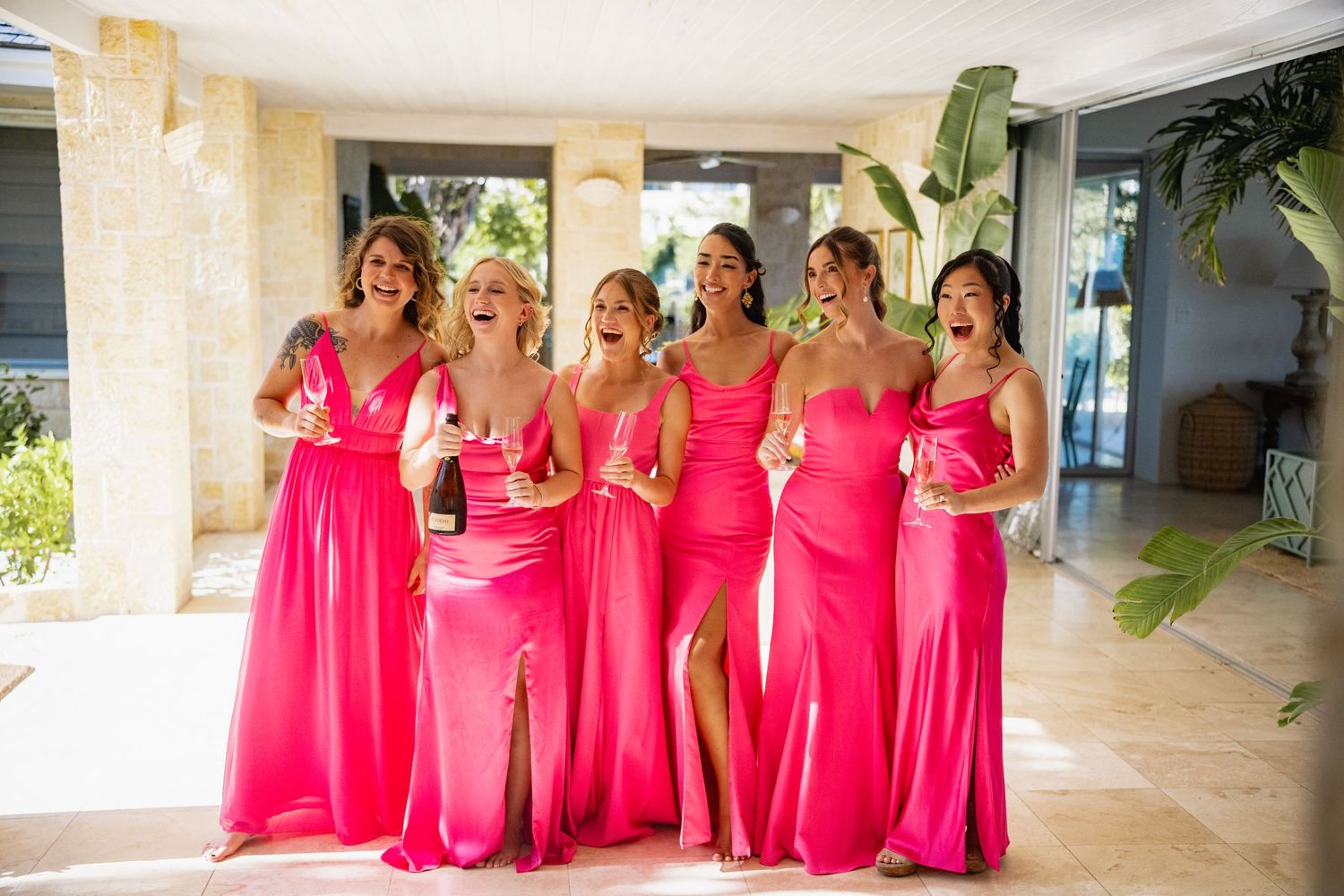 Group wearing vibrant pink formal dresses posing together on a covered patio.