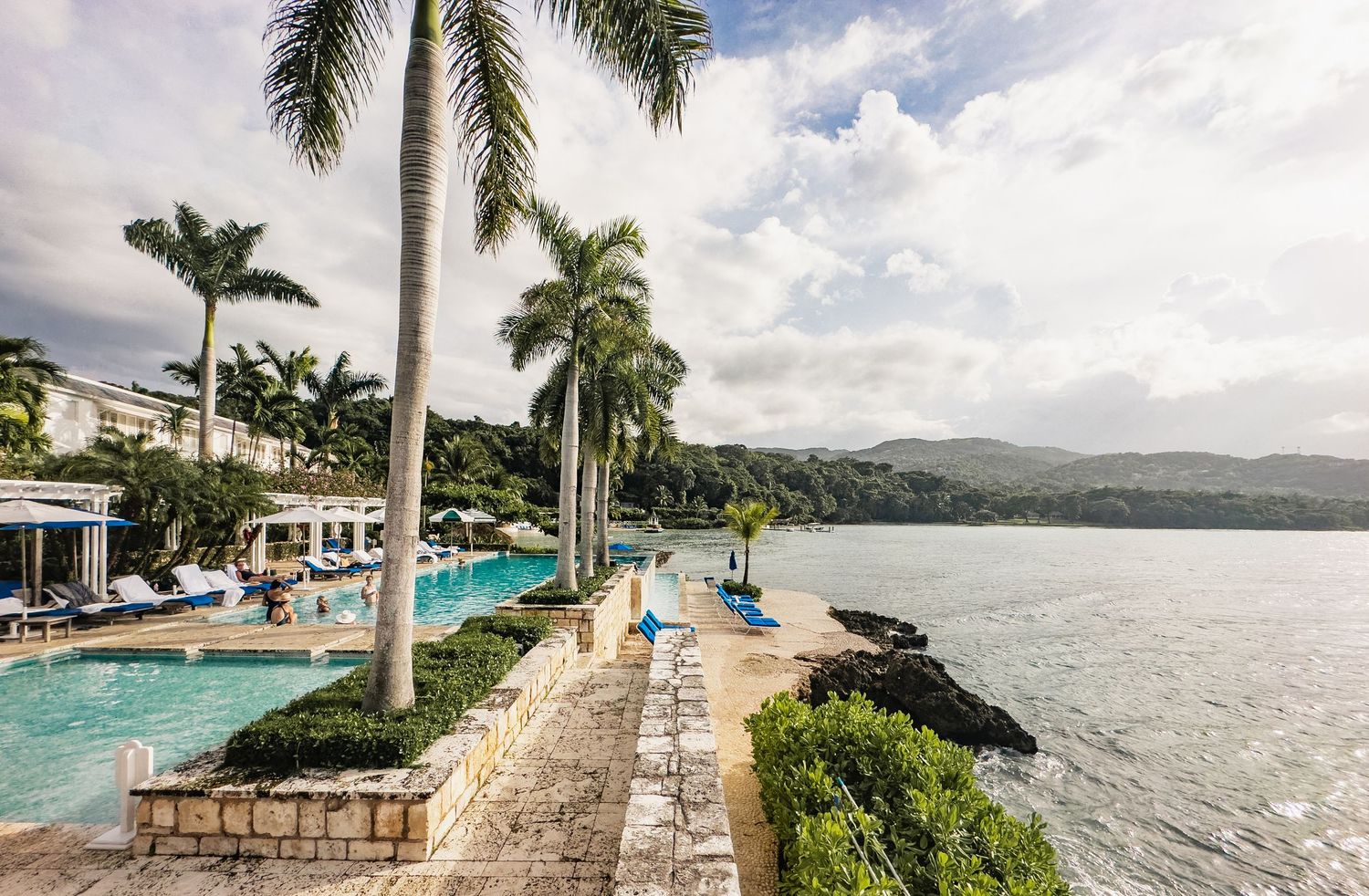 Panoramic view of a luxury beachfront resort with palm trees, swimming pools and ocean vistas in a tropical setting.