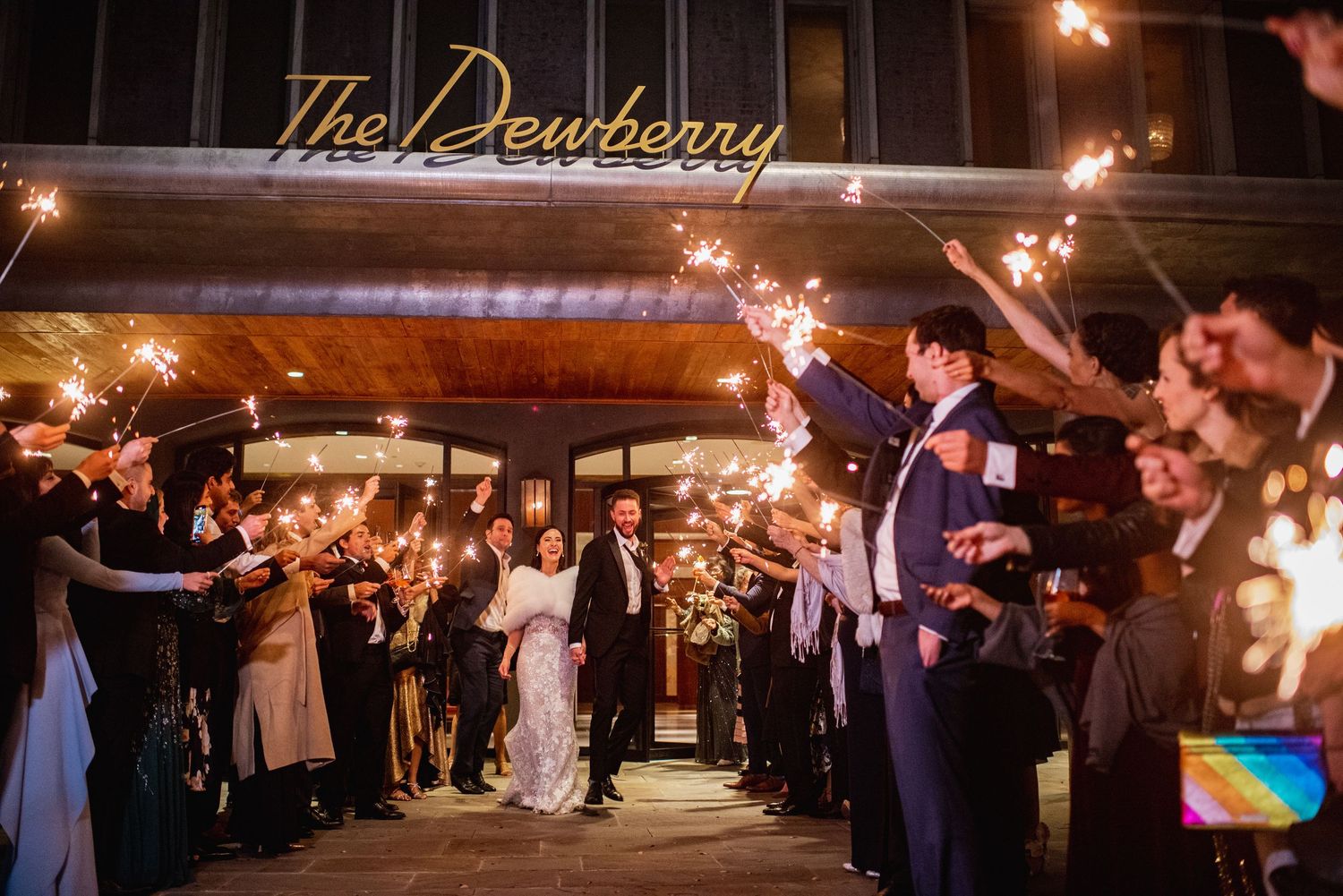 Wedding guests create a magical sparkler tunnel exit for newlyweds at an evening outdoor celebration.