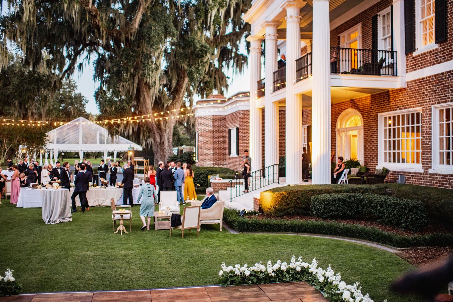 Elegant outdoor wedding venue with Spanish moss trees and white chairs arranged on a manicured lawn at sunset.