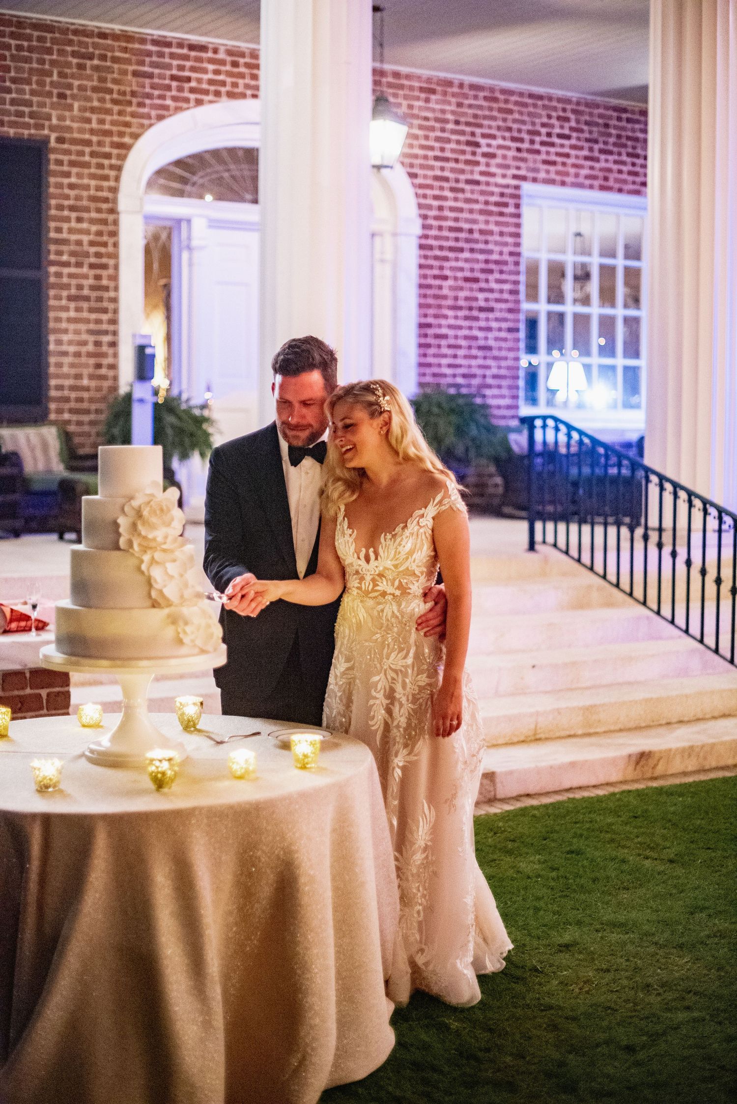 A couple shares a moment together at their wedding reception while cutting their elegant white tiered cake.