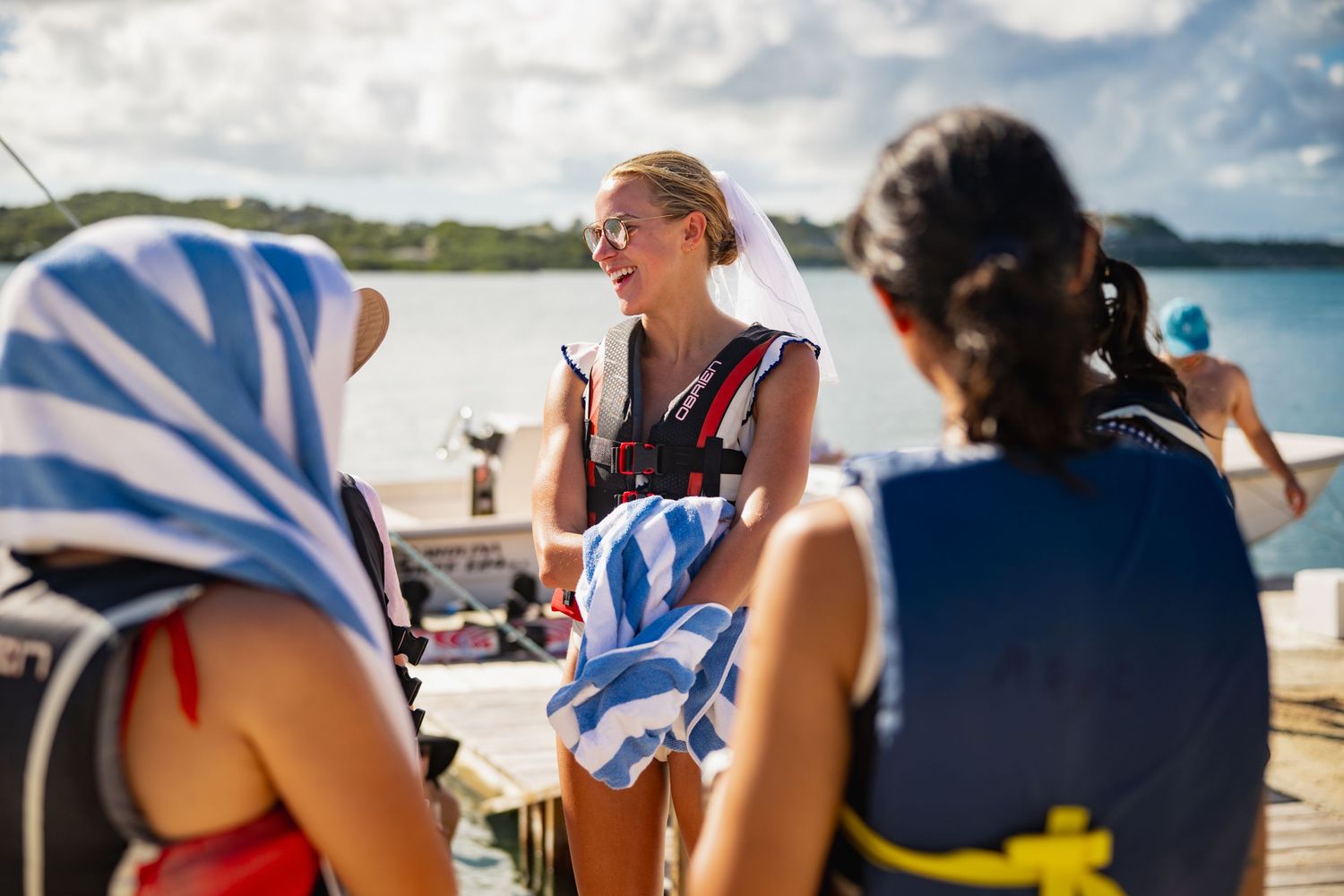 A group of people sitting in beach chairs along a tropical shoreline enjoying drinks and conversation on a sunny day.