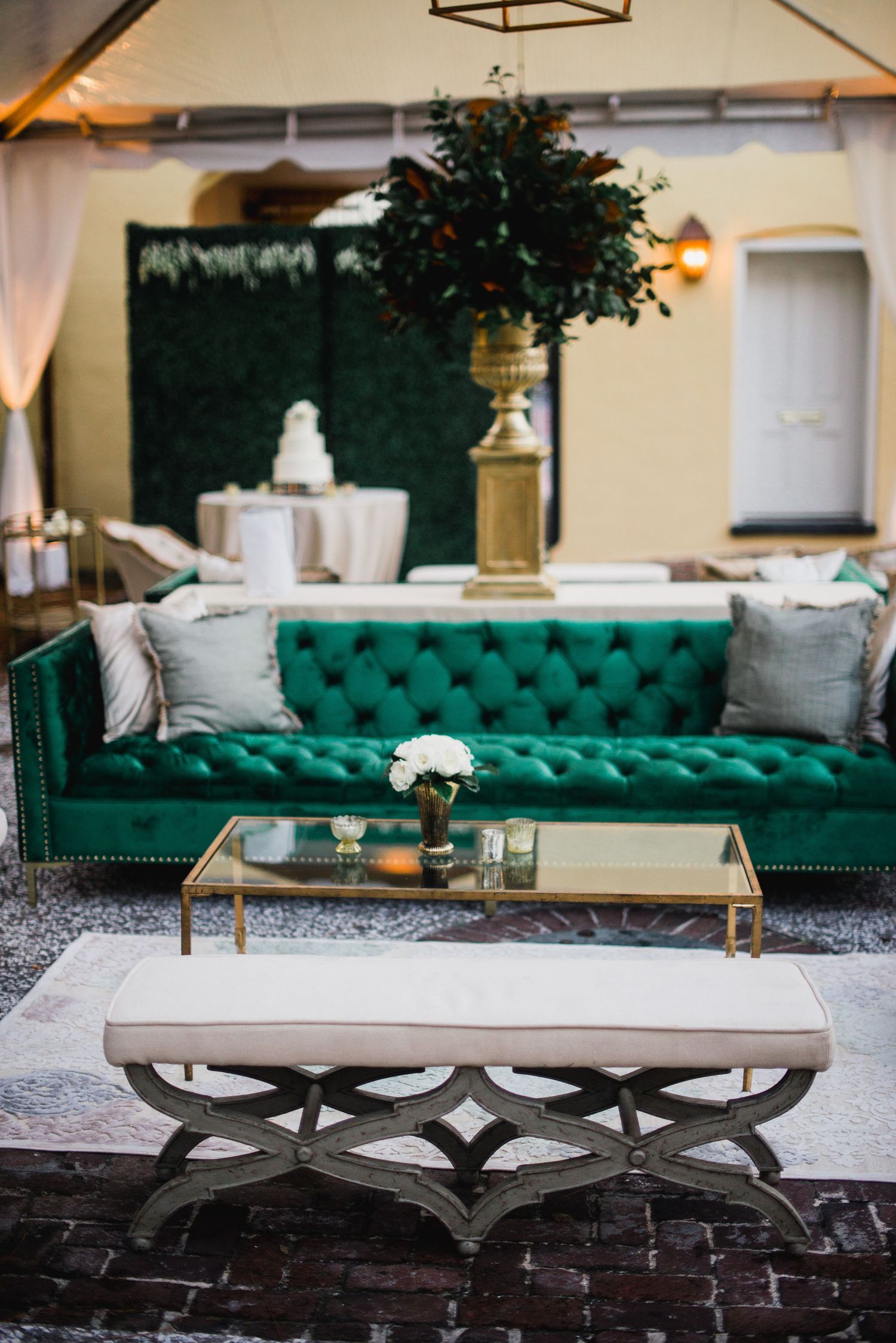 Elegant living room setup featuring a tufted emerald green velvet sofa with a modern glass coffee table on crossed legs.