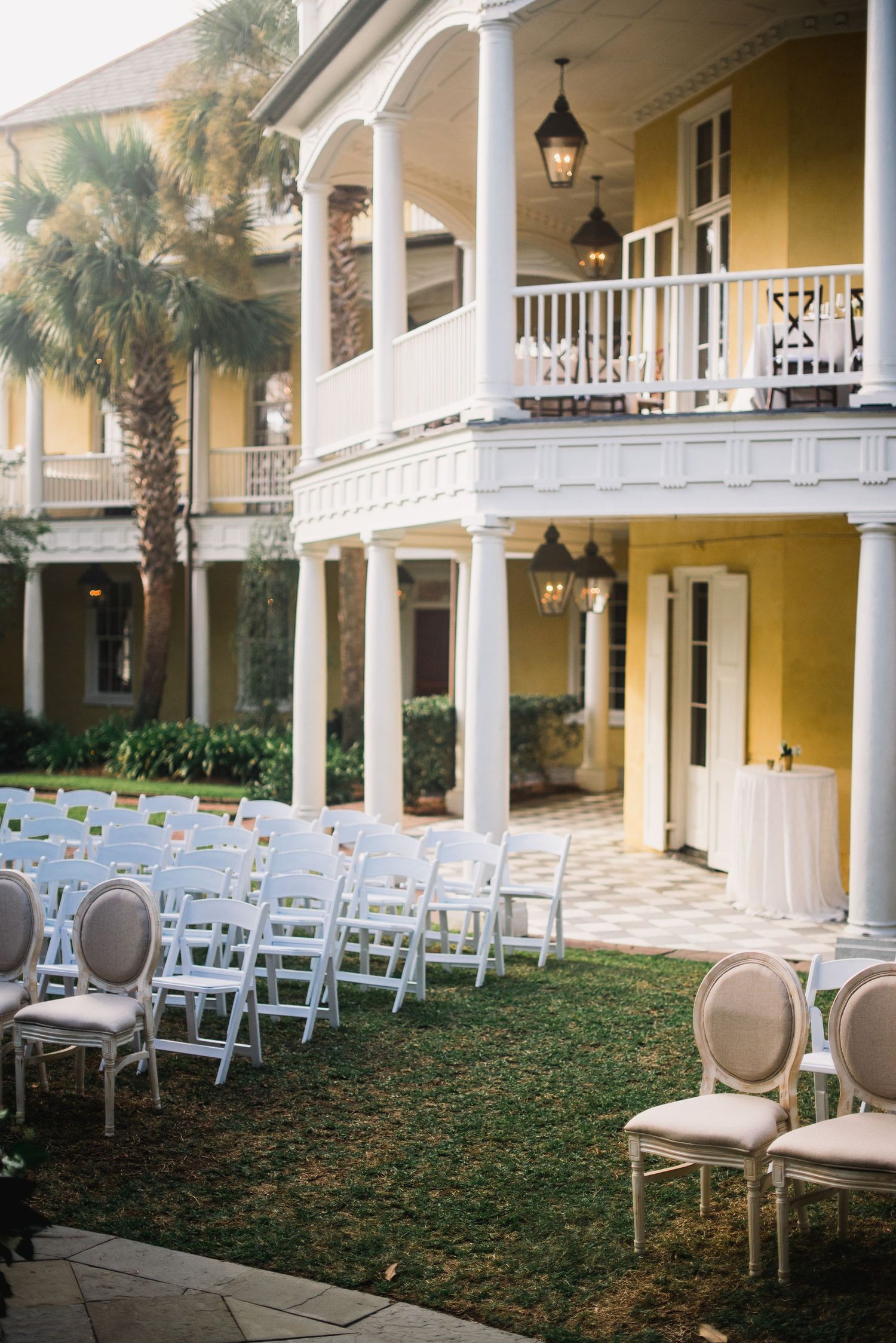 White chairs arranged for an outdoor wedding ceremony at a Southern plantation-style venue with yellow walls and white columns.