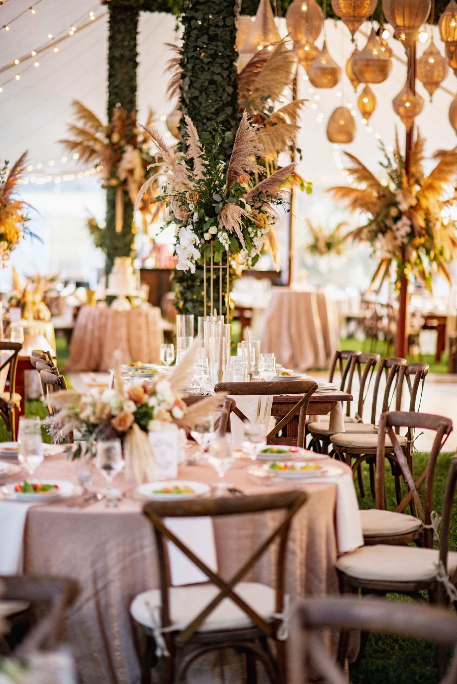 Elegant wedding reception tables decorated with white linens, string lights, and hanging woven lanterns create a romantic atmosphere.