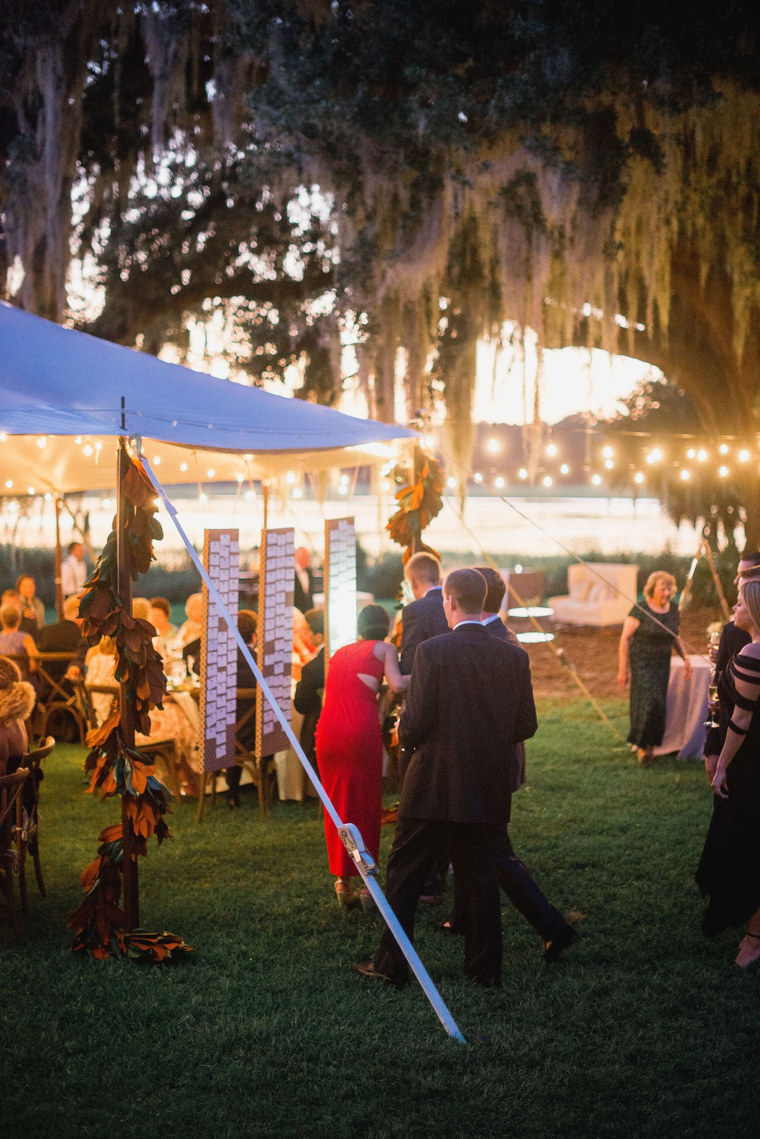 Silhouettes of people with glowing lightsabers gather at an outdoor evening event with string lights and trees.