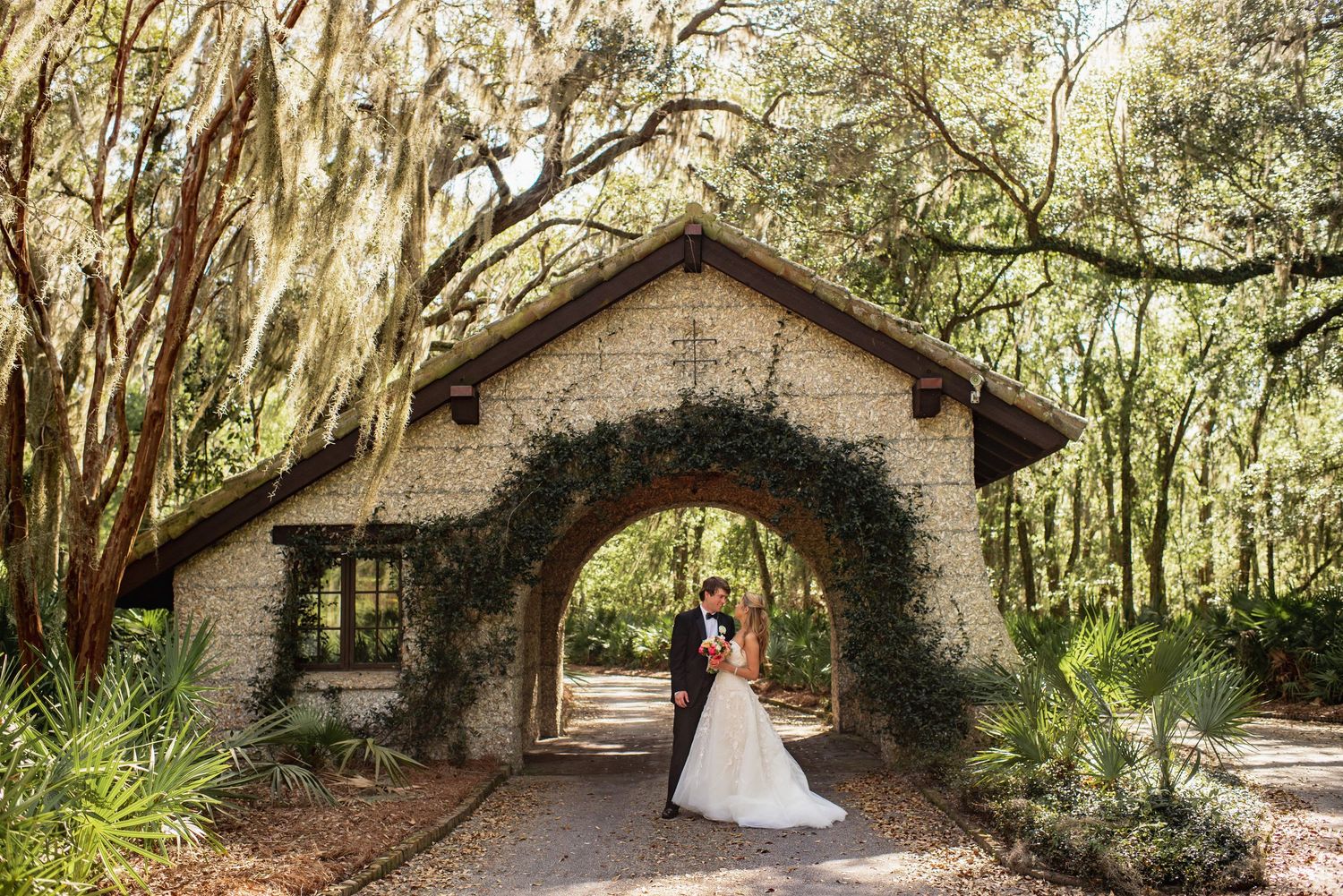 Romantic wedding photos taken under a natural archway of Spanish moss-draped oak trees at a southern garden venue.