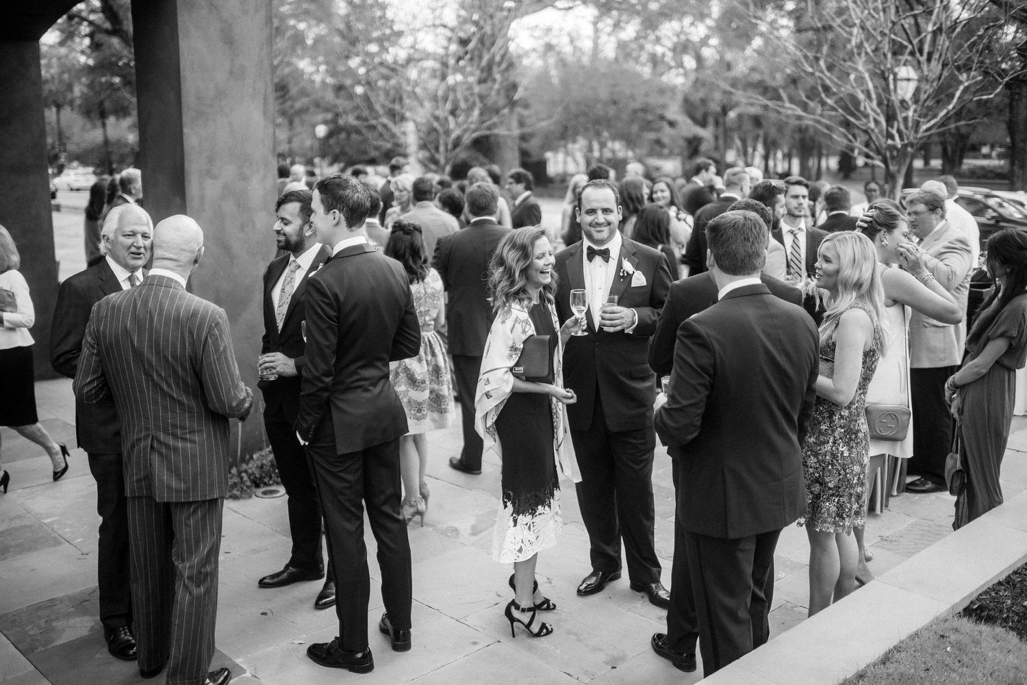 Wedding guests mingle and socialize during an outdoor reception in a garden setting.