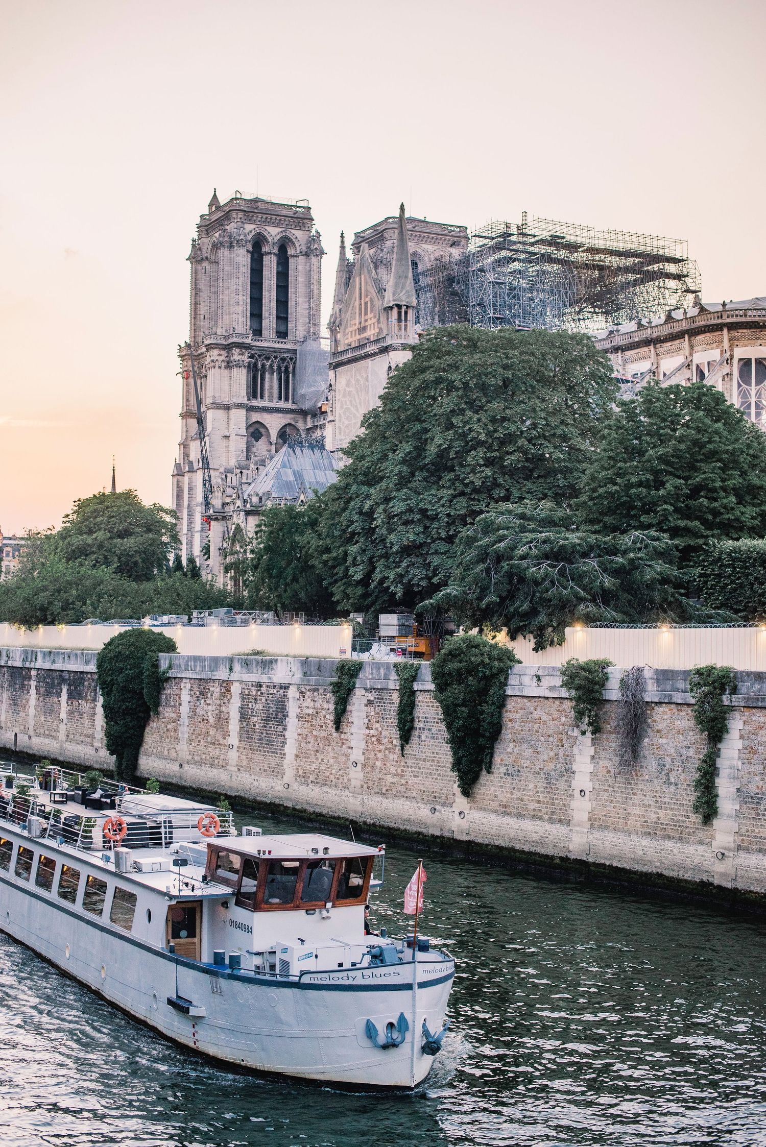Tour boats cruise along the Seine River past Notre-Dame Cathedral in Paris during sunset.