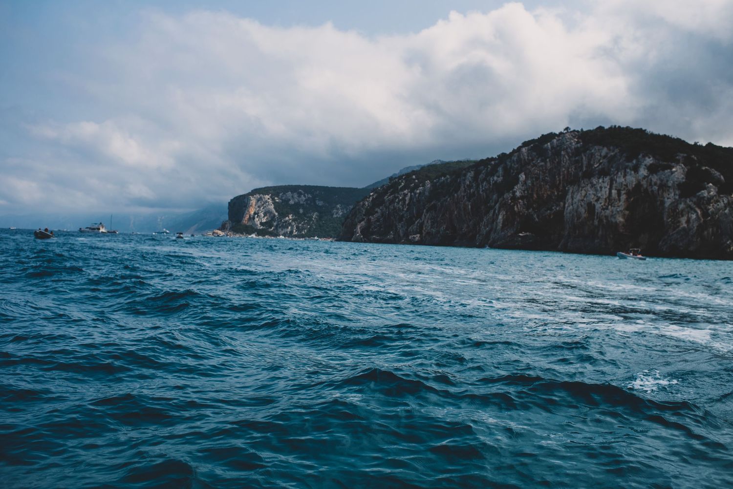 Dramatic seascape of rocky cliffs along a choppy blue ocean under moody cloudy skies.