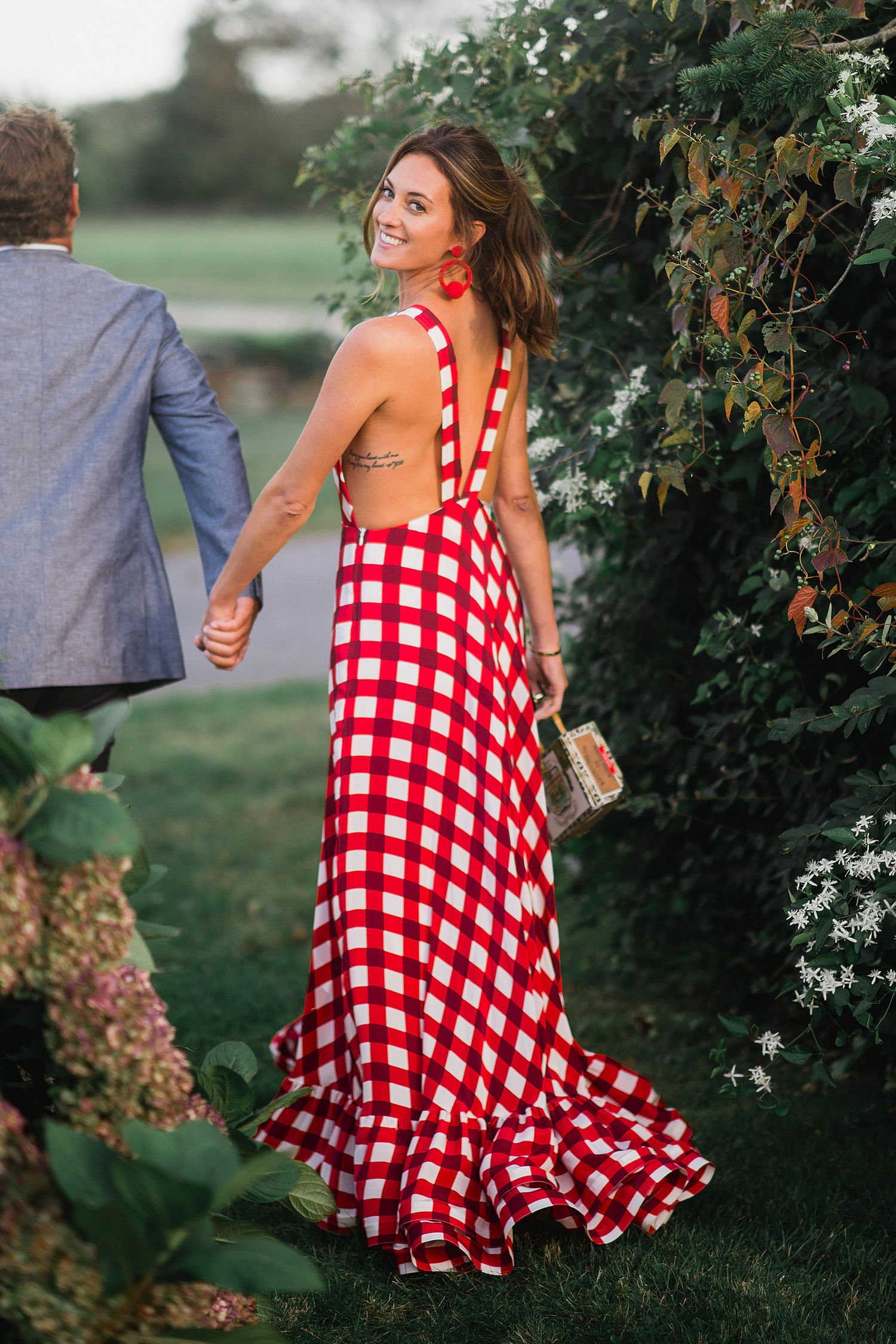 Person wearing a flowing red and white gingham dress twirling in a garden setting.