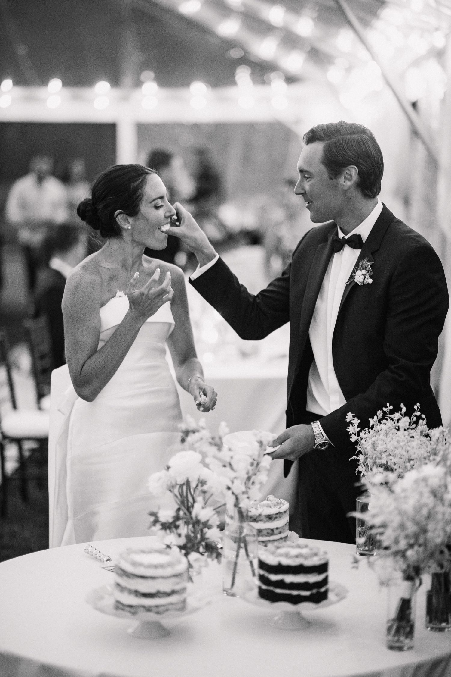 A joyful moment at a wedding reception as newlyweds share cake by their dessert table decorated with flowers.