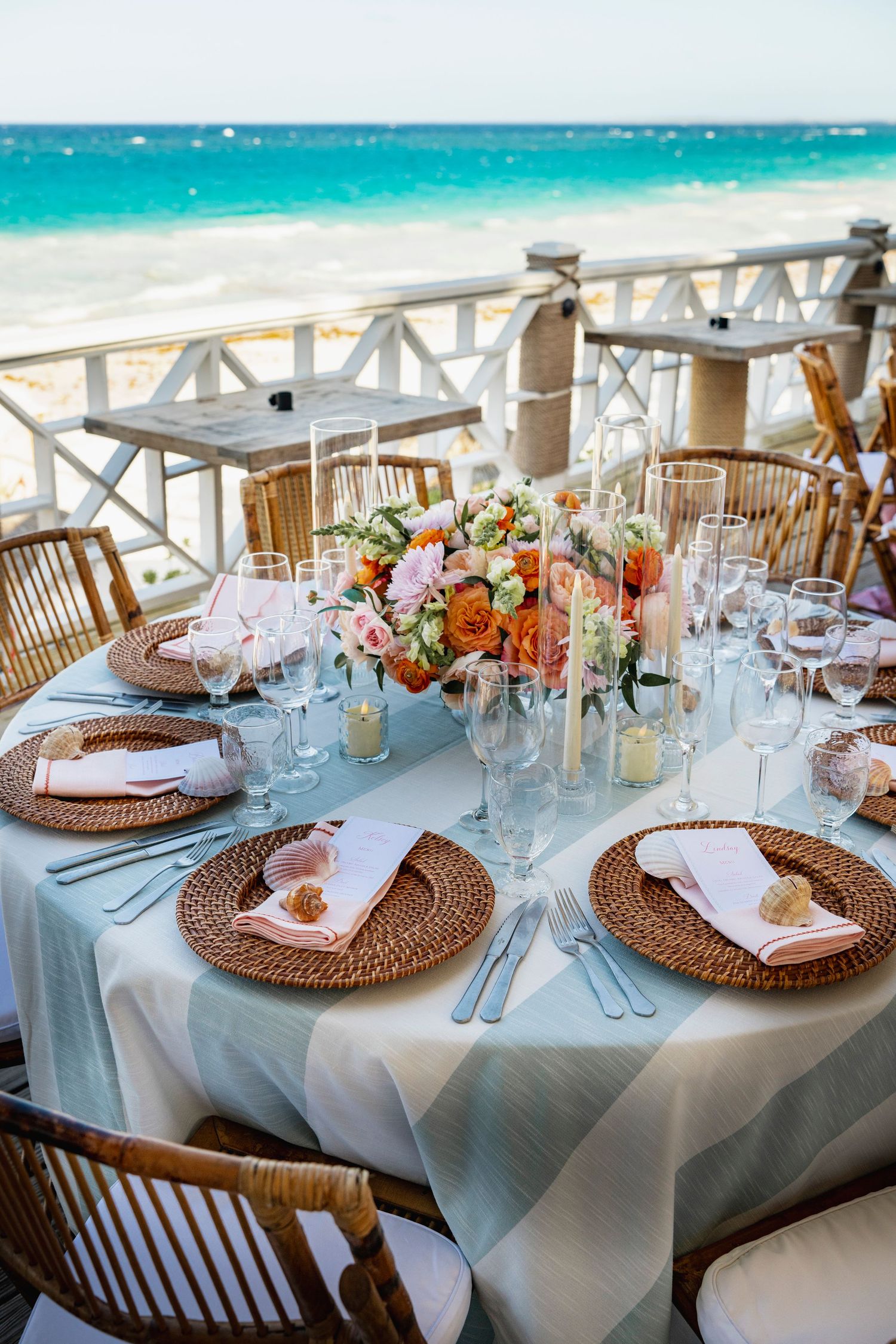 Elegant beach wedding reception table with woven chargers and floral centerpiece overlooking turquoise waters.