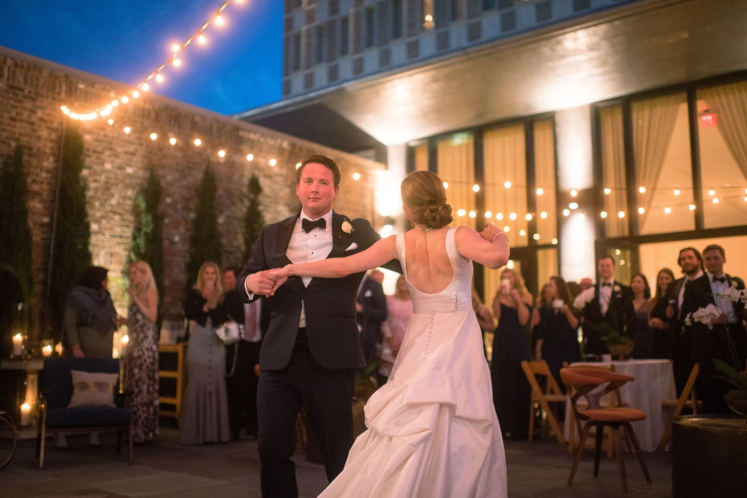 Wedding guests dance and celebrate under string lights at an outdoor evening reception venue.