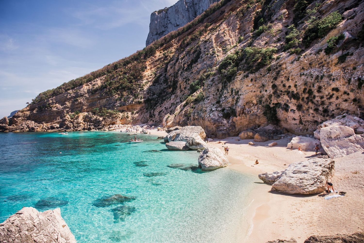 Crystal clear turquoise waters meet dramatic rocky cliffs along a pristine Sardinia coastline.