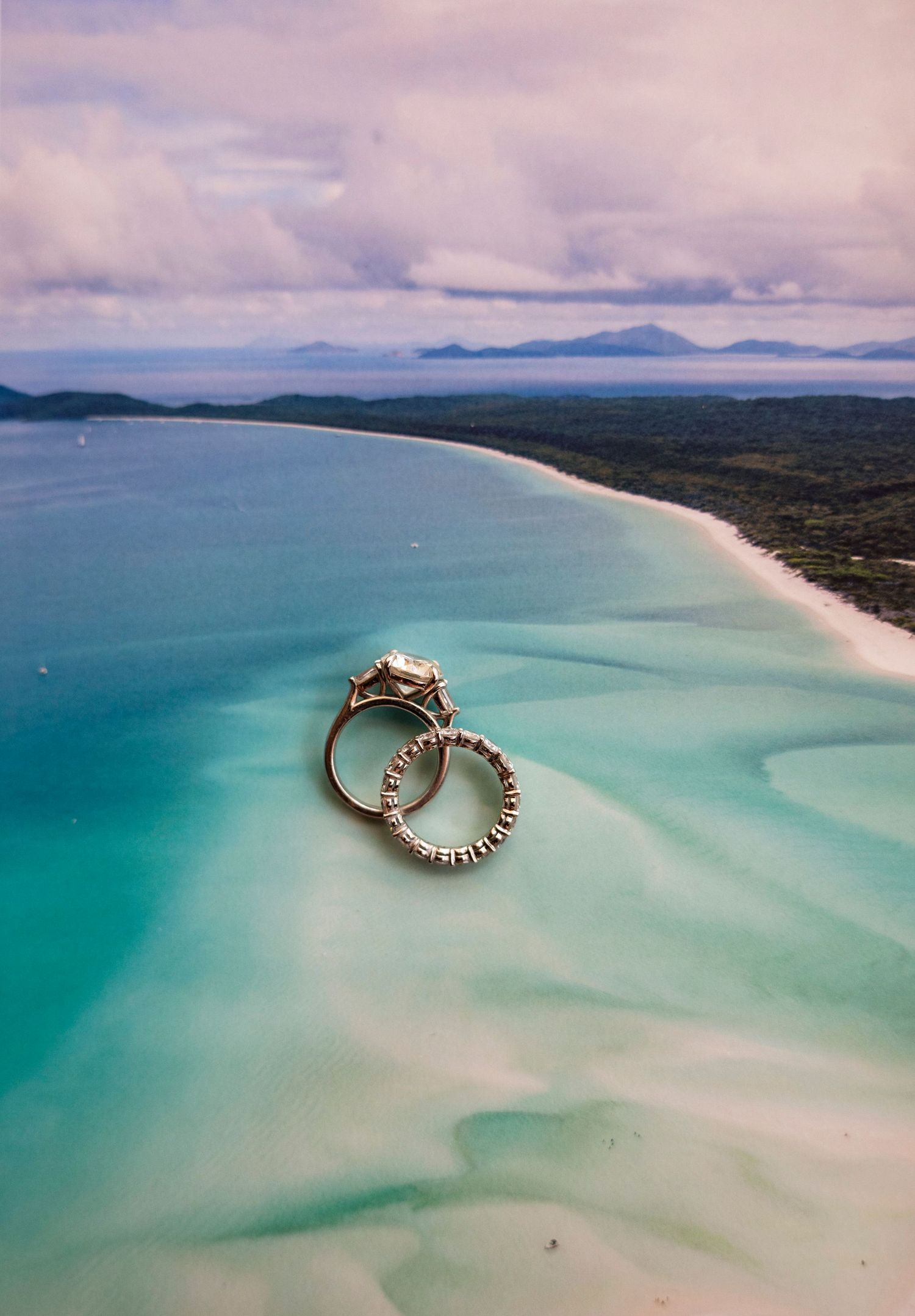 Aerial view of Whitehaven Beach in Australia showing pristine turquoise waters meeting white sandy shoreline under cloudy skies.