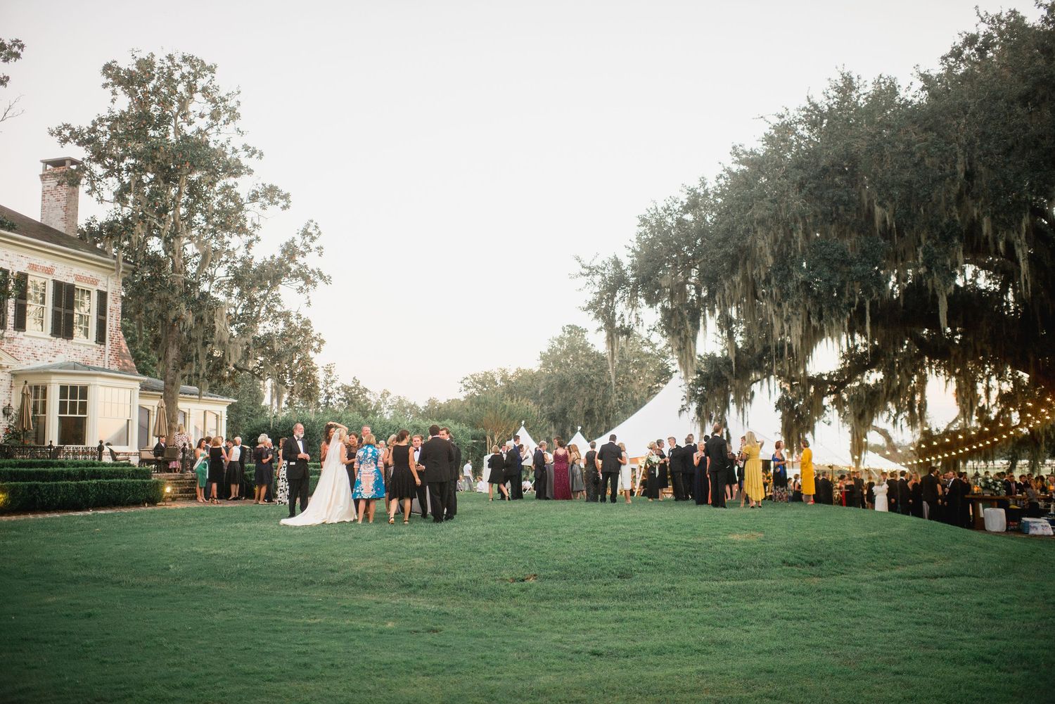 A panoramic view of an outdoor wedding ceremony set against a backdrop of lush trees and elegant architecture.