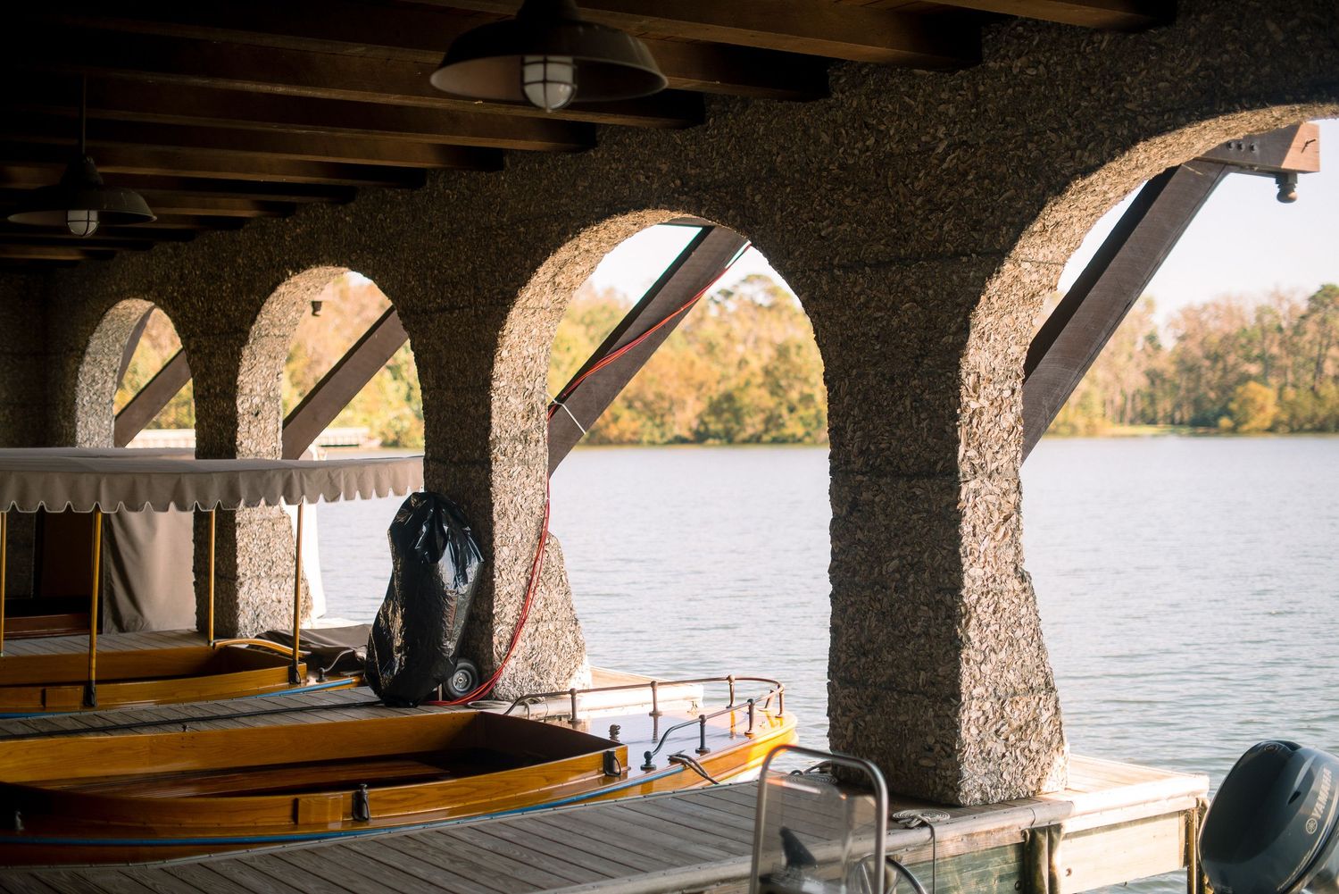 Scenic lakeside view through stone archways with wooden beams and benches creating a covered waterfront promenade.