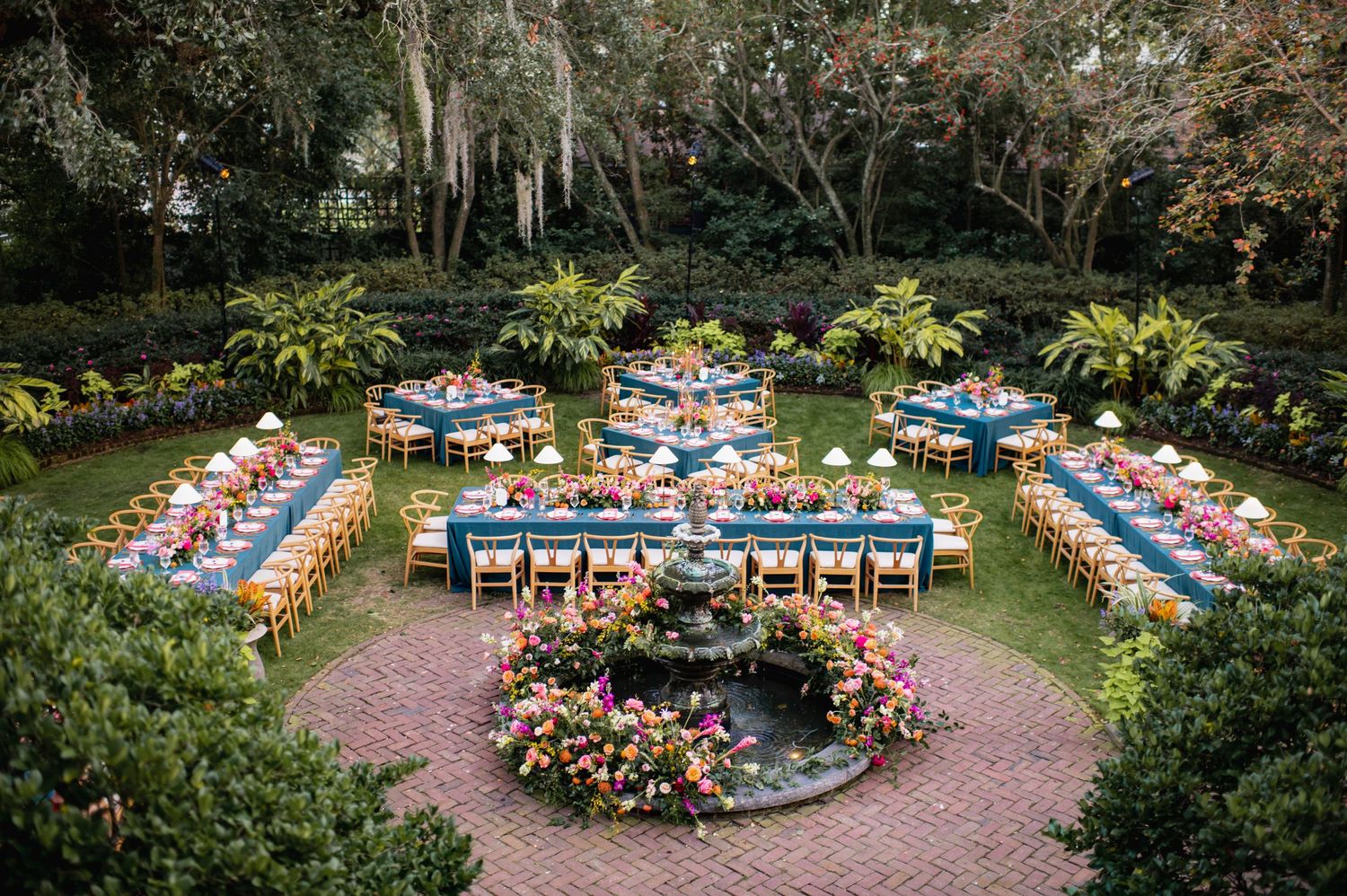 Elegant outdoor wedding reception tables decorated with blue linens and floral centerpieces in a garden setting.