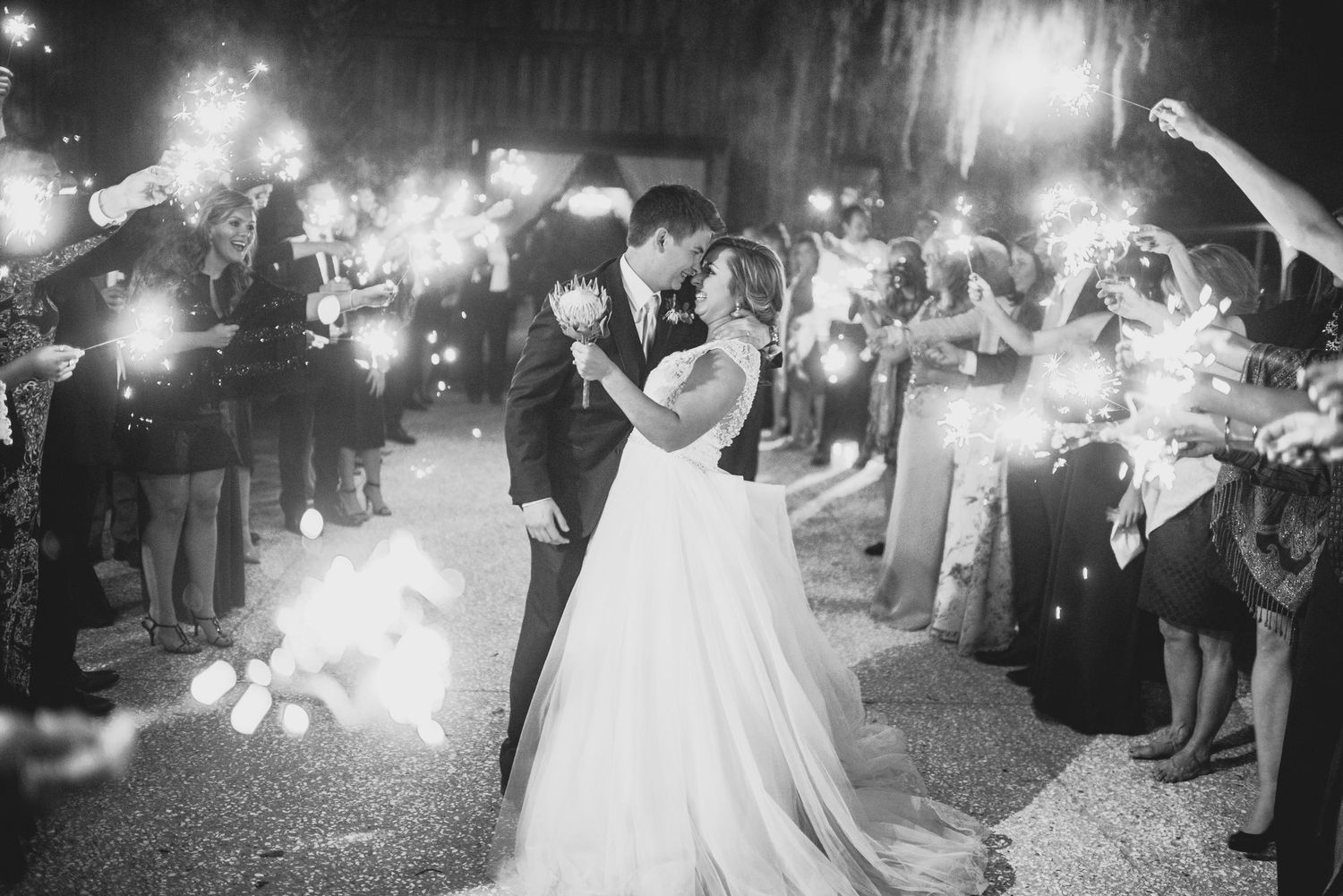 Wedding couple dances surrounded by guests holding sparklers creating a magical nighttime celebration atmosphere.