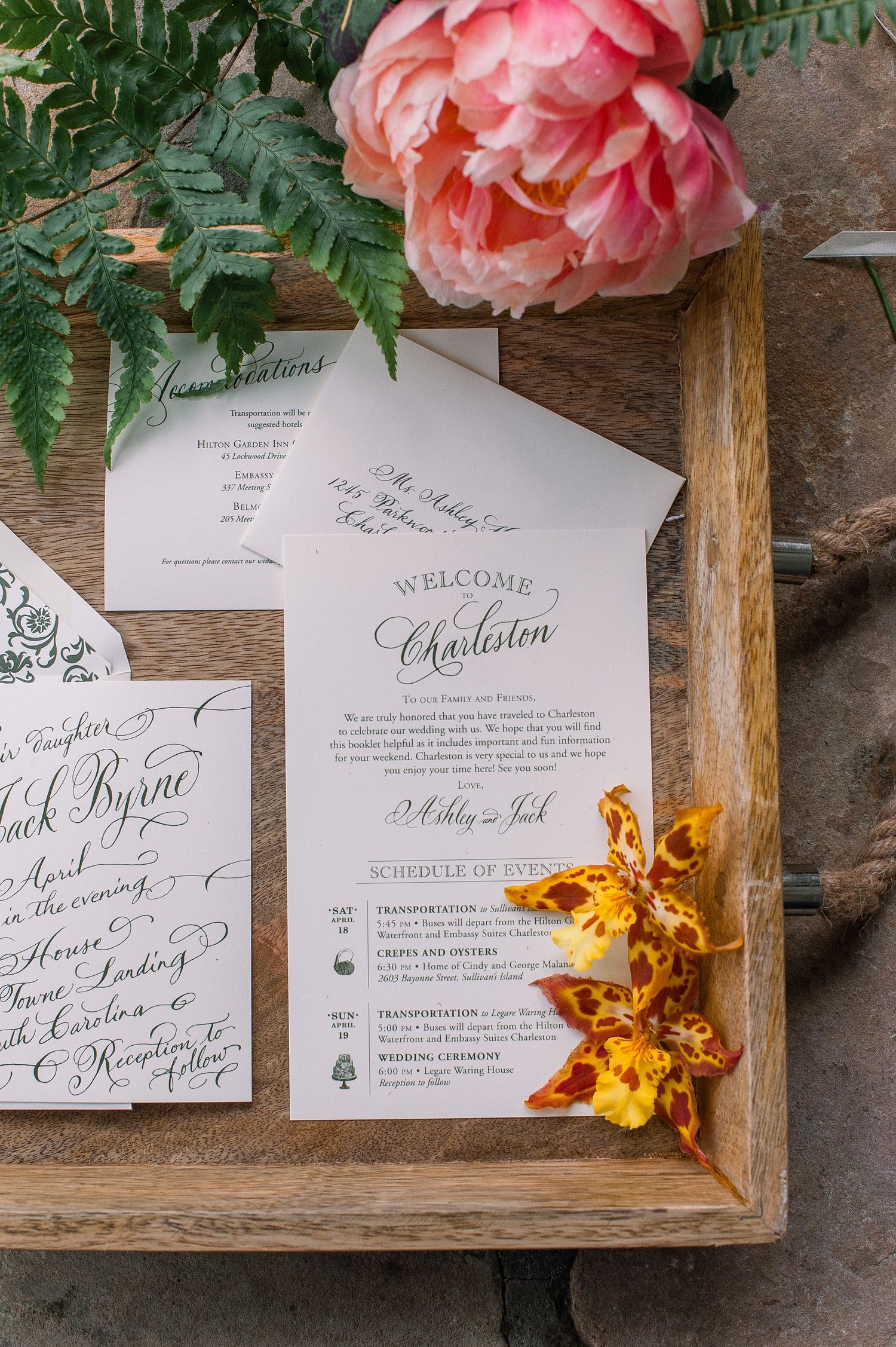 Elegant wedding invitation suite with pink peony flower and gold accents displayed on wooden tray.