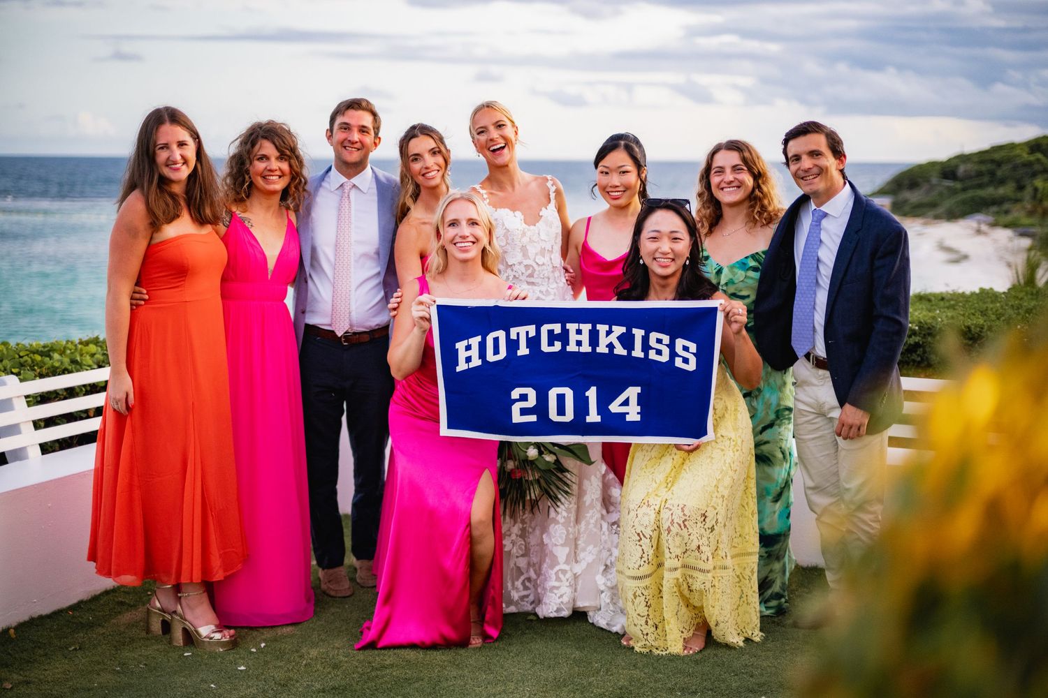 Group photo with bright pink and coral dresses against a scenic coastal backdrop.