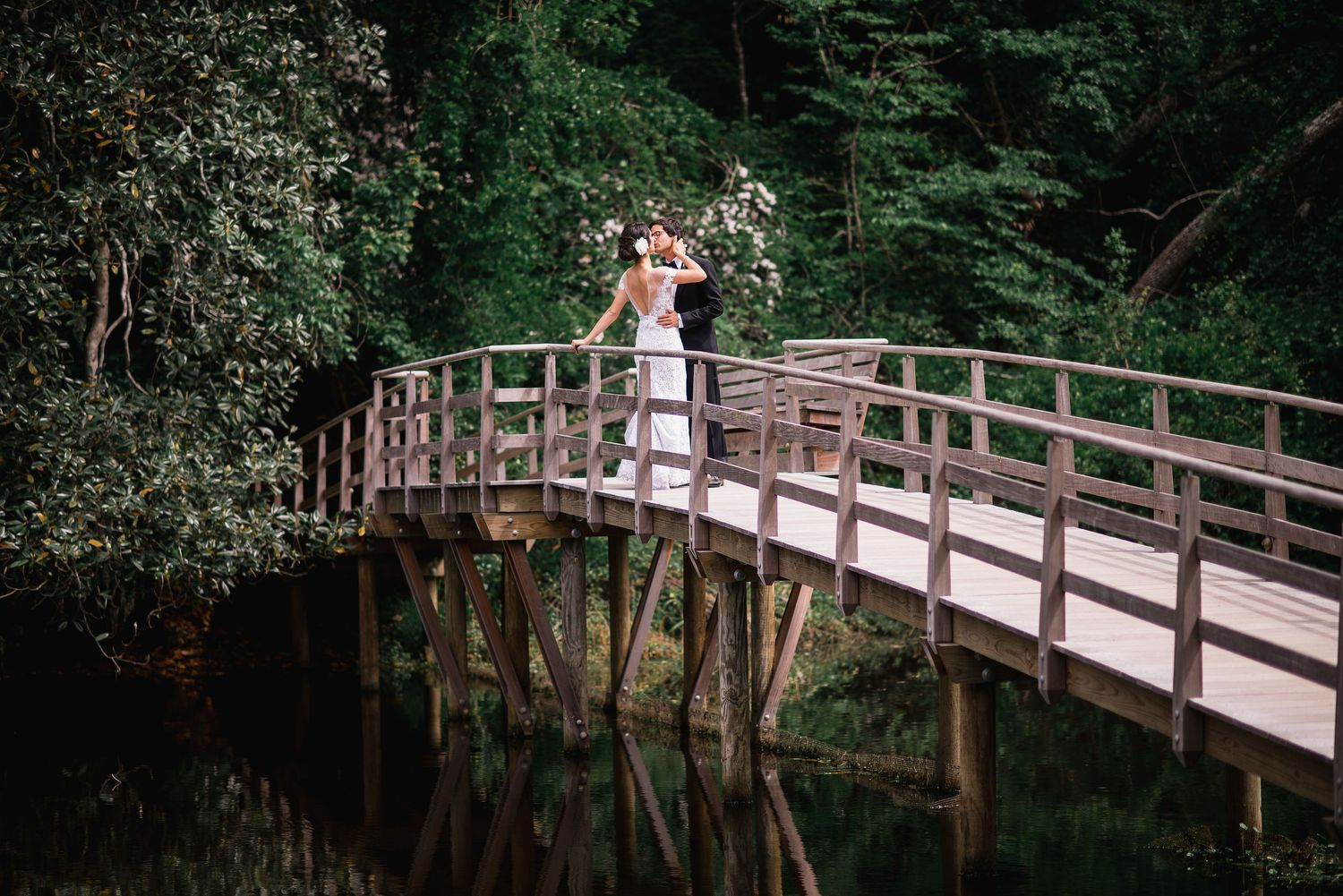 A couple stands on a rustic wooden bridge in a lush forest setting during a romantic photoshoot.