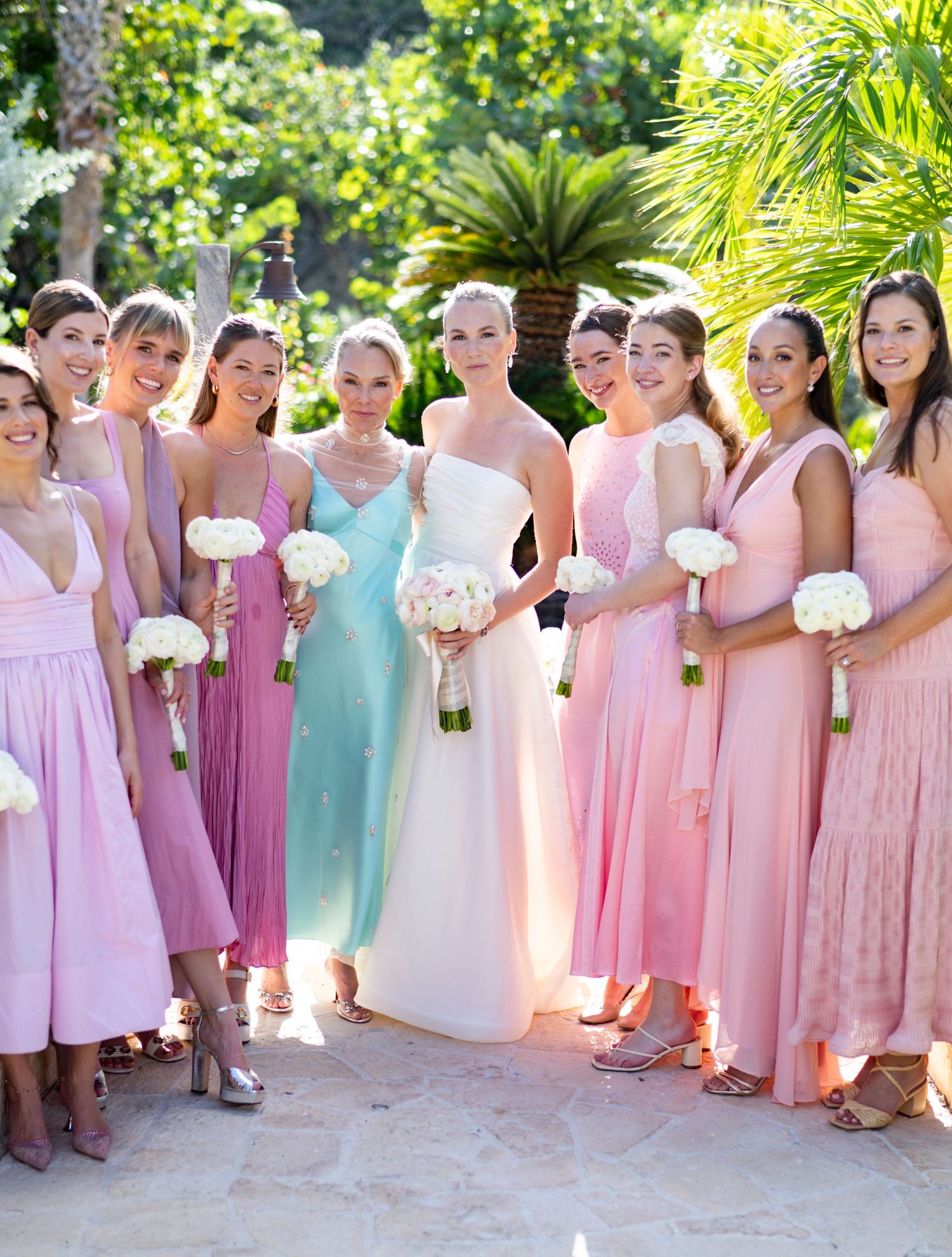 Bridesmaids wearing pastel pink and mint dresses pose with bouquets in a garden setting.