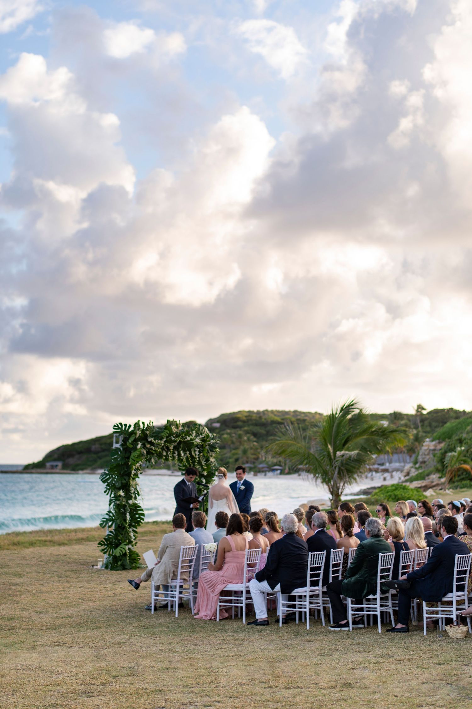 Outdoor wedding ceremony setup with white chairs facing the ocean under cloudy skies.