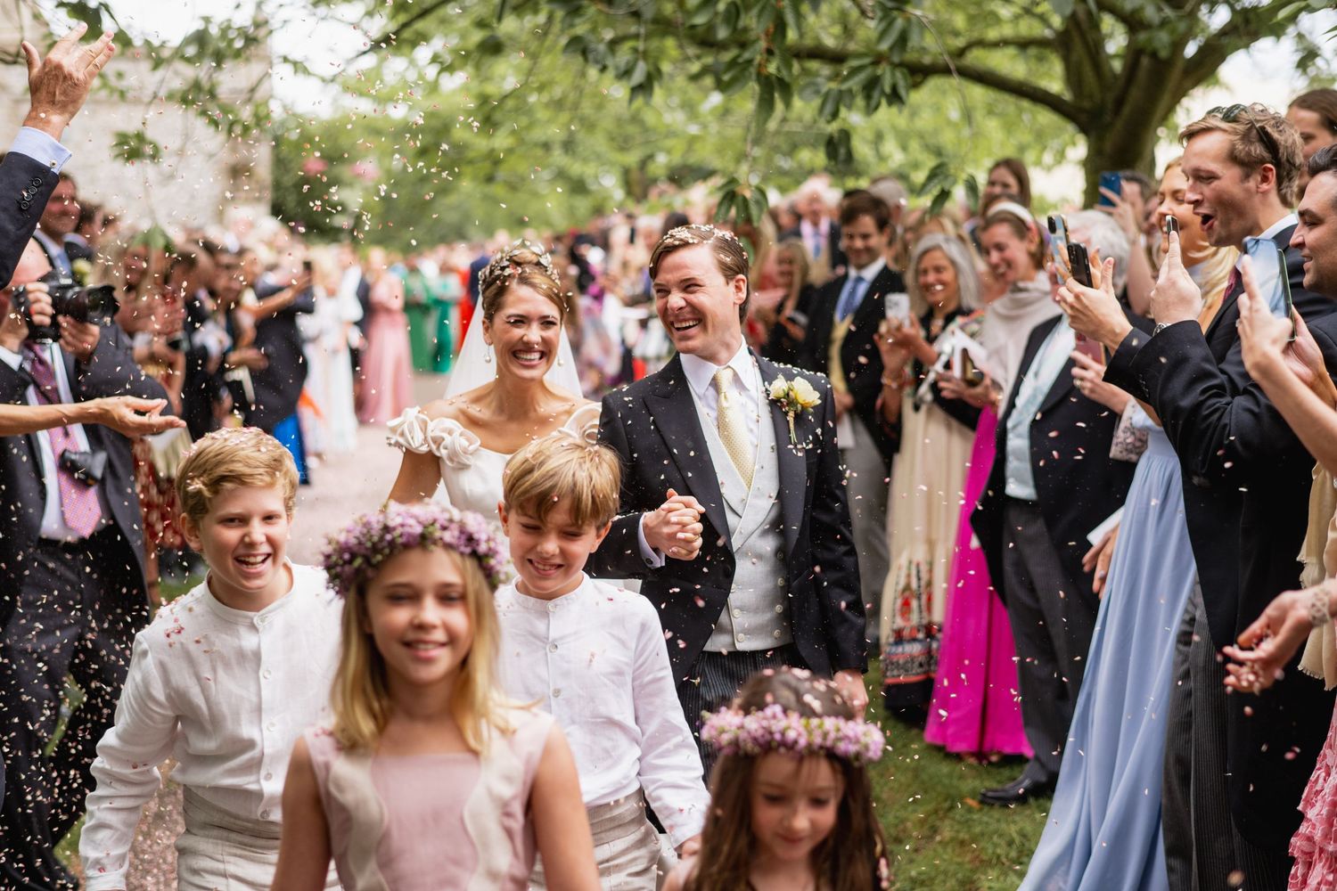 Wedding guests celebrate outdoors by throwing flower petals and confetti during a joyful ceremony exit.