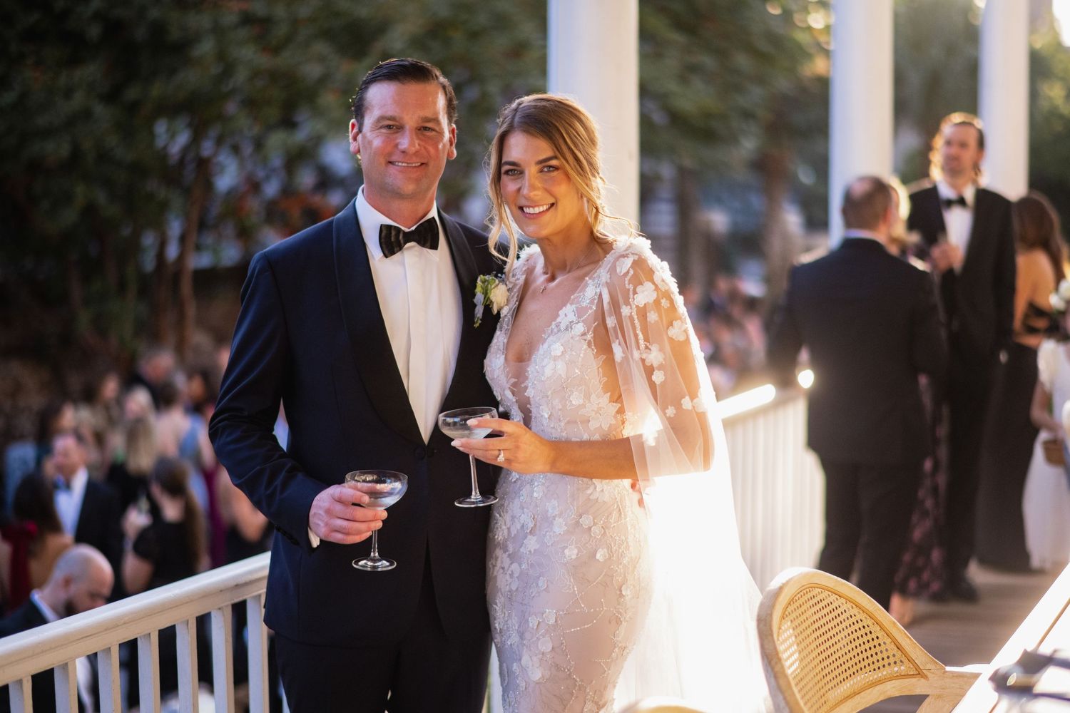Elegant wedding couple sharing romantic moments at an outdoor reception with string lights and natural scenery.