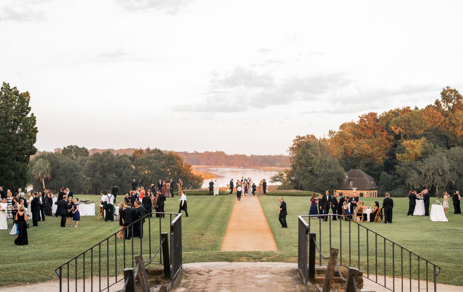 Panoramic view of an outdoor wedding venue with guests gathered on a grassy hillside at sunset.