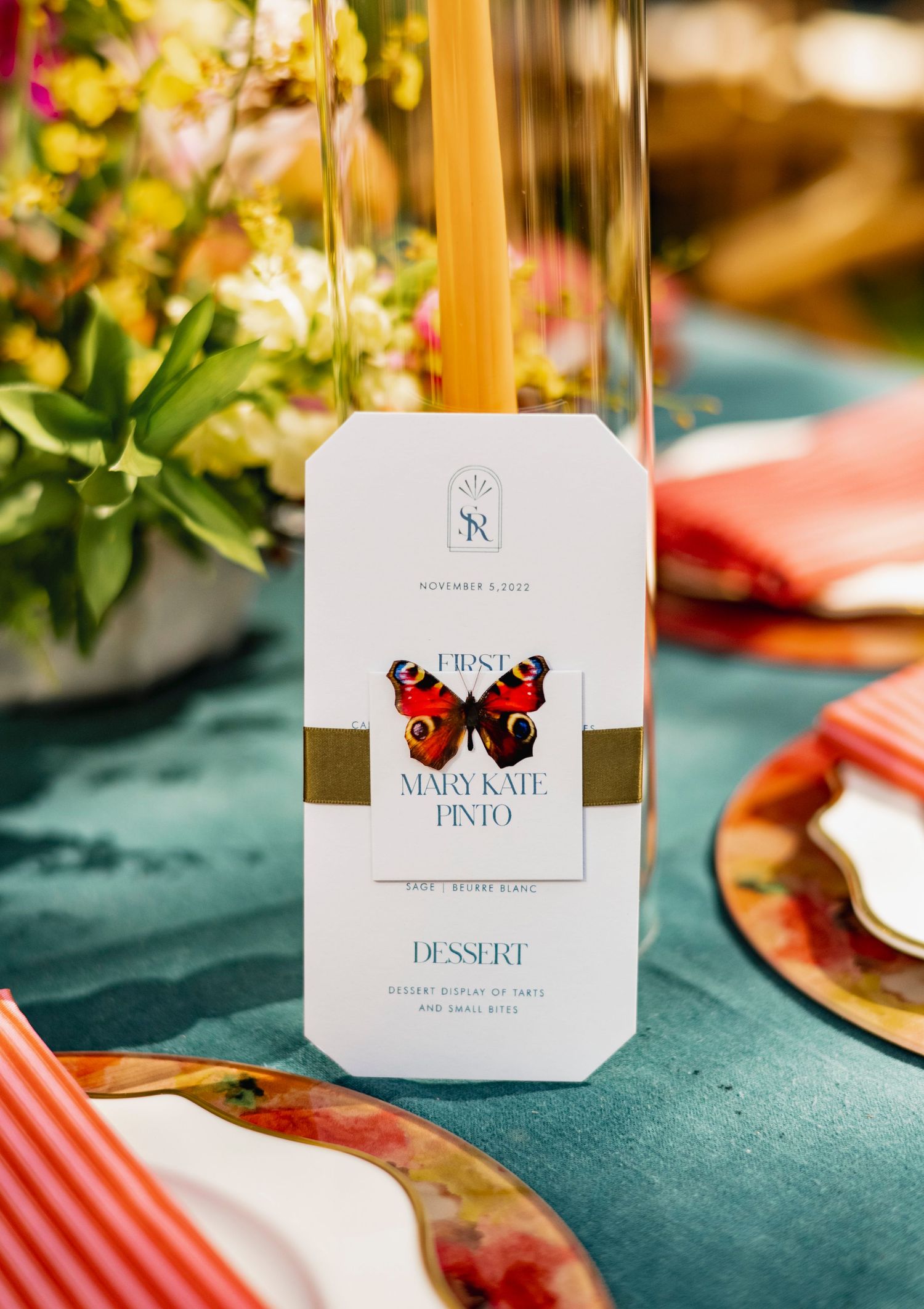 Wedding reception table settings with elegant place cards, floral centerpieces, and teal and coral color scheme details.