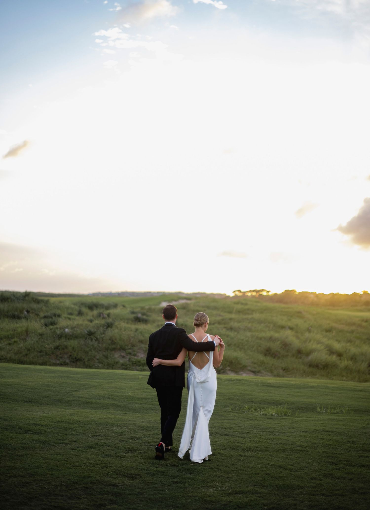A couple walks together on a grassy hillside at sunset creating a romantic silhouette against the sky.