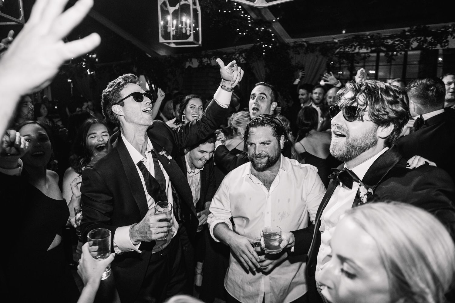 A black and white photograph of people celebrating at a lively party with drinks in their hands.