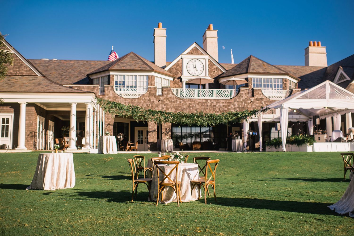 A panoramic view of an elegant outdoor wedding venue setup with white chairs and decor against a classic mansion backdrop.