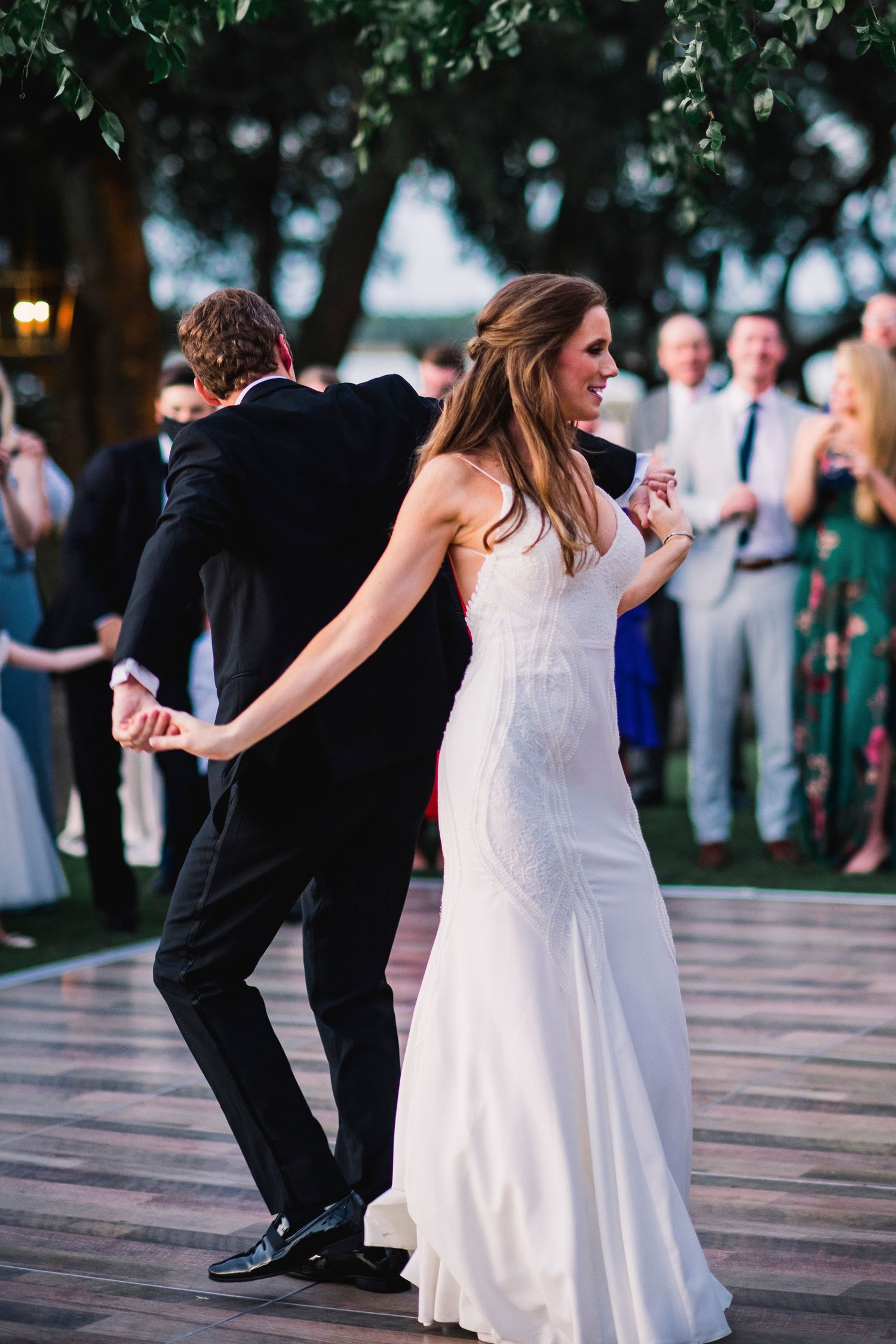 Wedding guests dancing together on an outdoor wooden deck during an evening celebration.