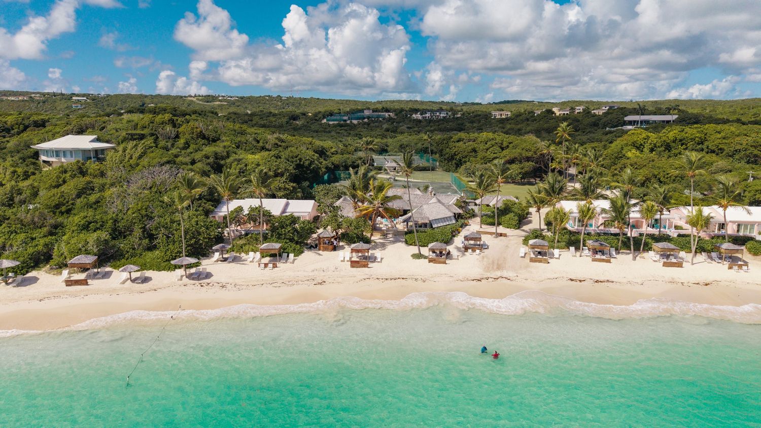 Tropical beachfront panorama with palm trees and turquoise waters under white puffy clouds at the Mill Reef club, Antigua