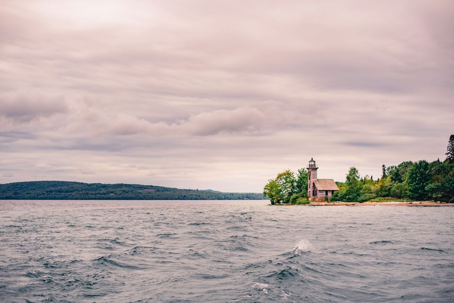 Panoramic seascape with cloudy skies and distant lighthouse on a coastal headland.