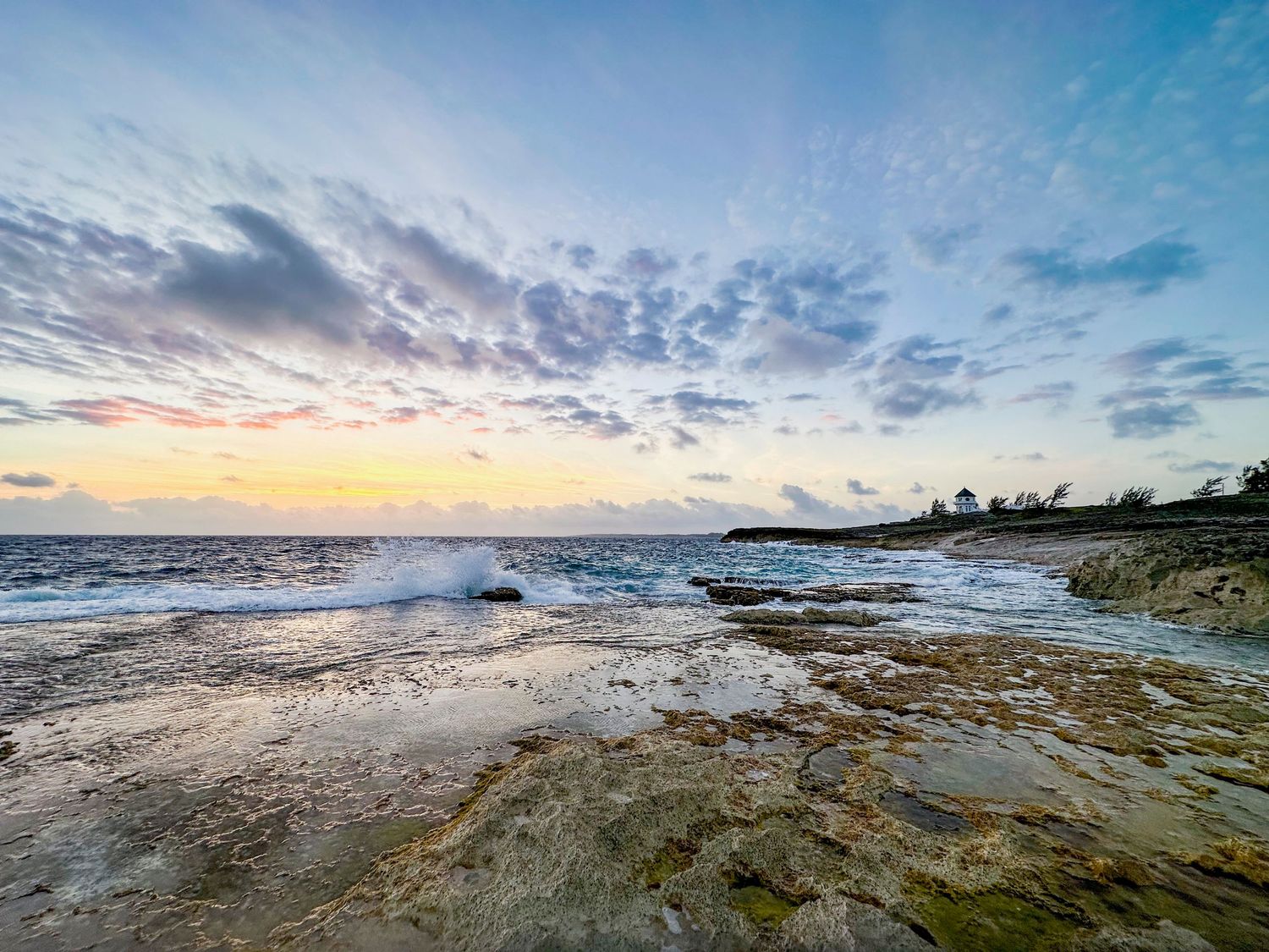 Wide panoramic view of a rocky beach coastline during sunset with dramatic cloud formations.