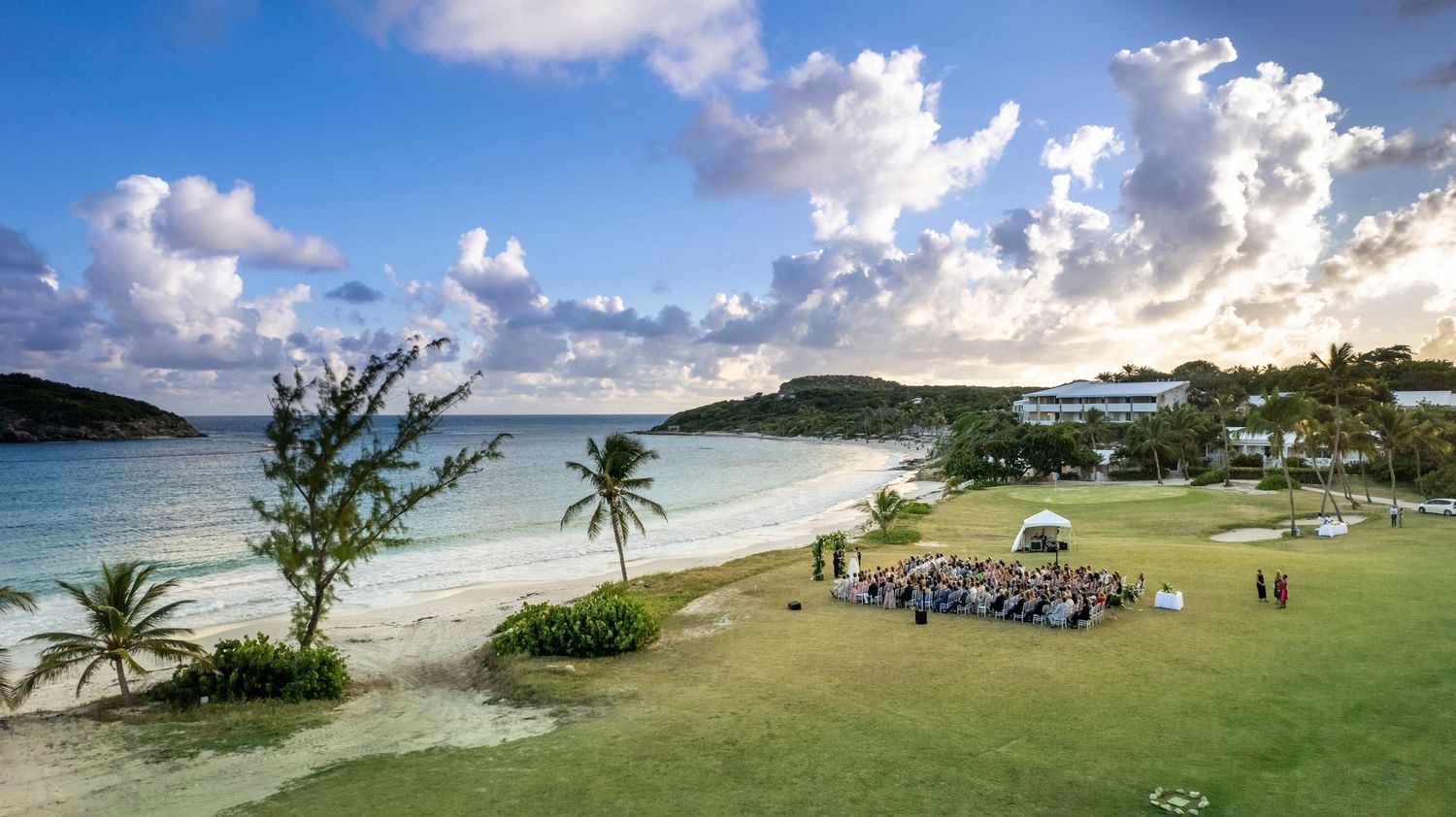 Panoramic view of a tropical beach with palm trees and turquoise waters under a dramatic cloudy sky.