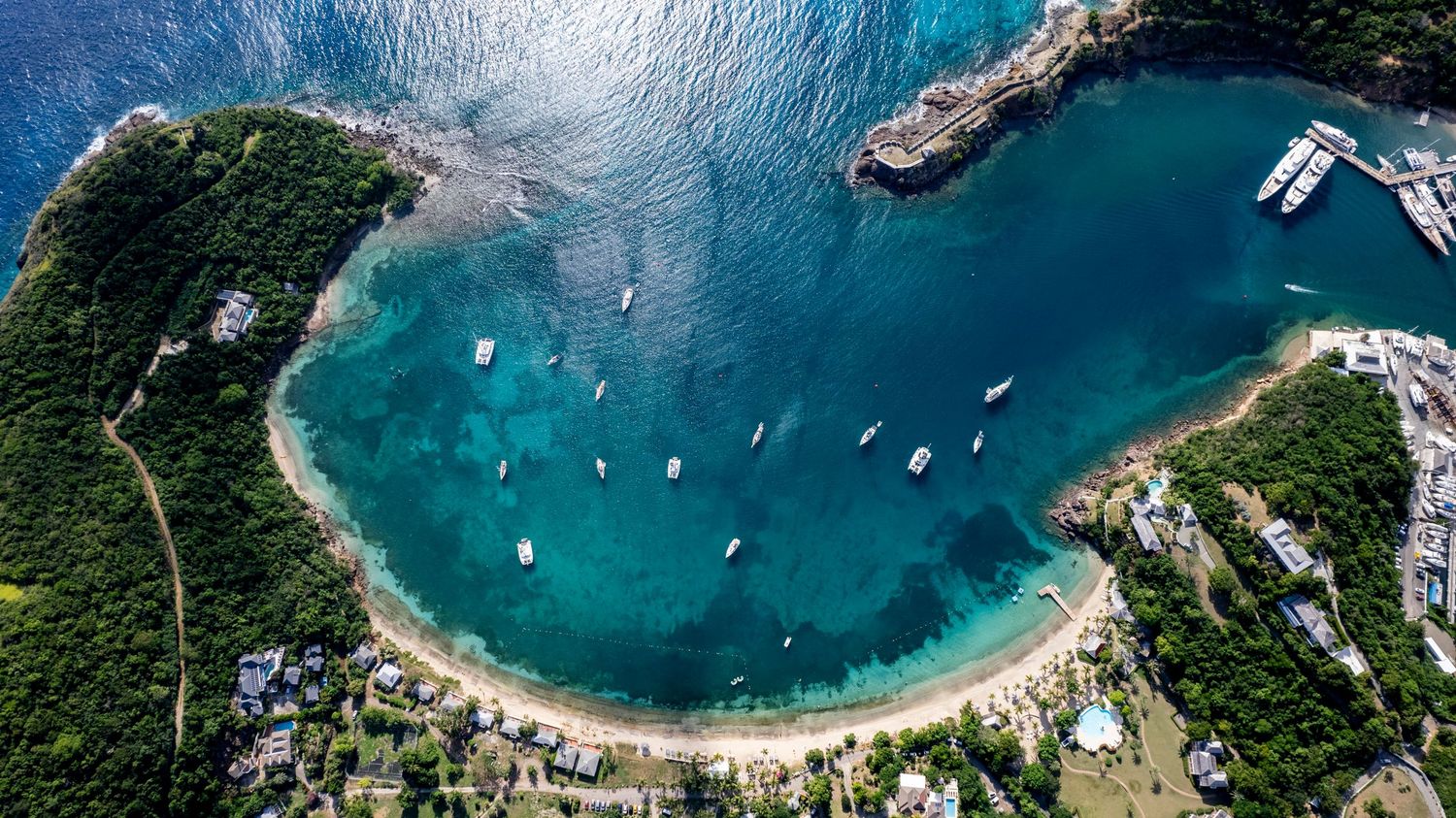 Aerial panoramic view of a tropical bay with turquoise waters, boats, and lush green coastline.
