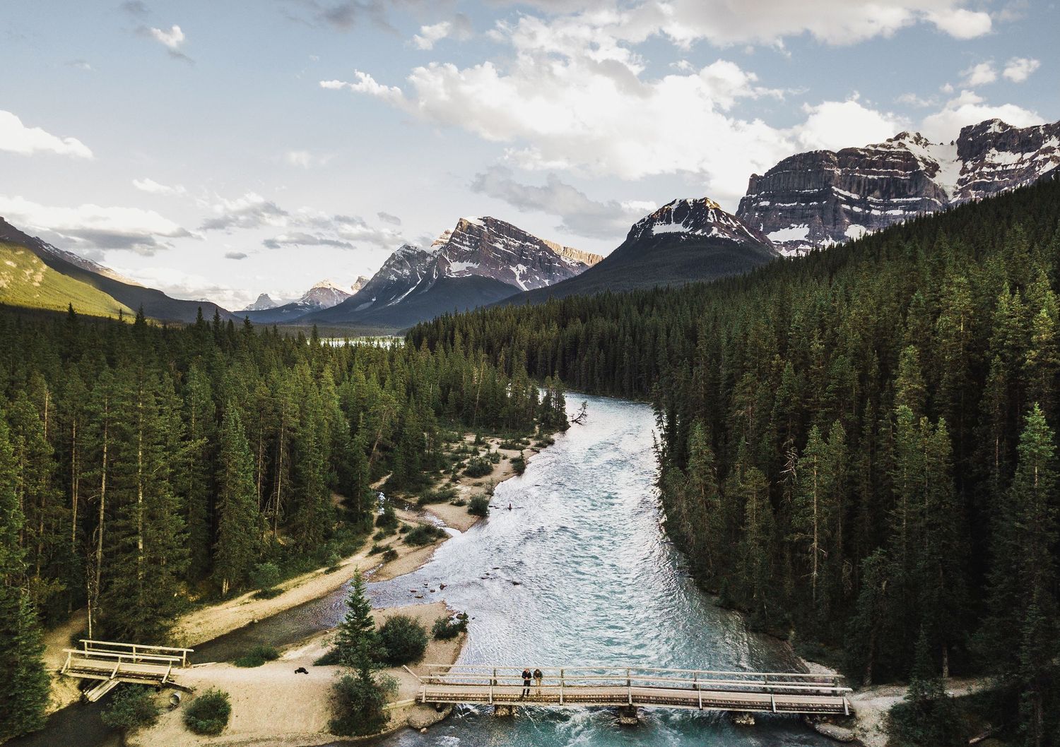Scenic mountain river winding through evergreen forest with bridge crossing in Banff National Park.